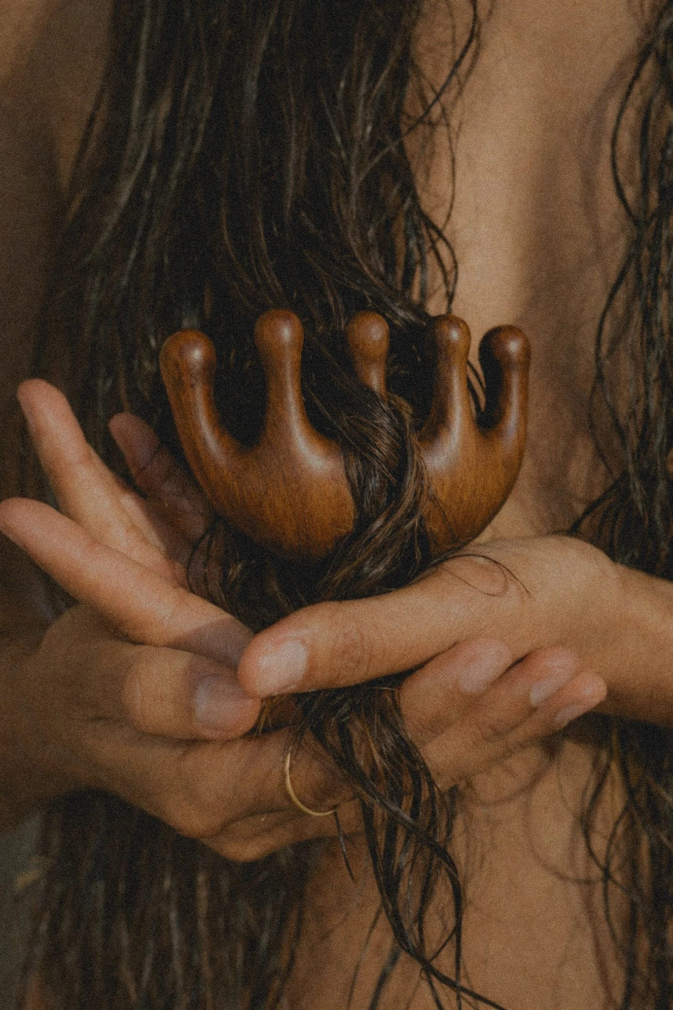 A person with wet hair holding a wooden comb close to their neck.