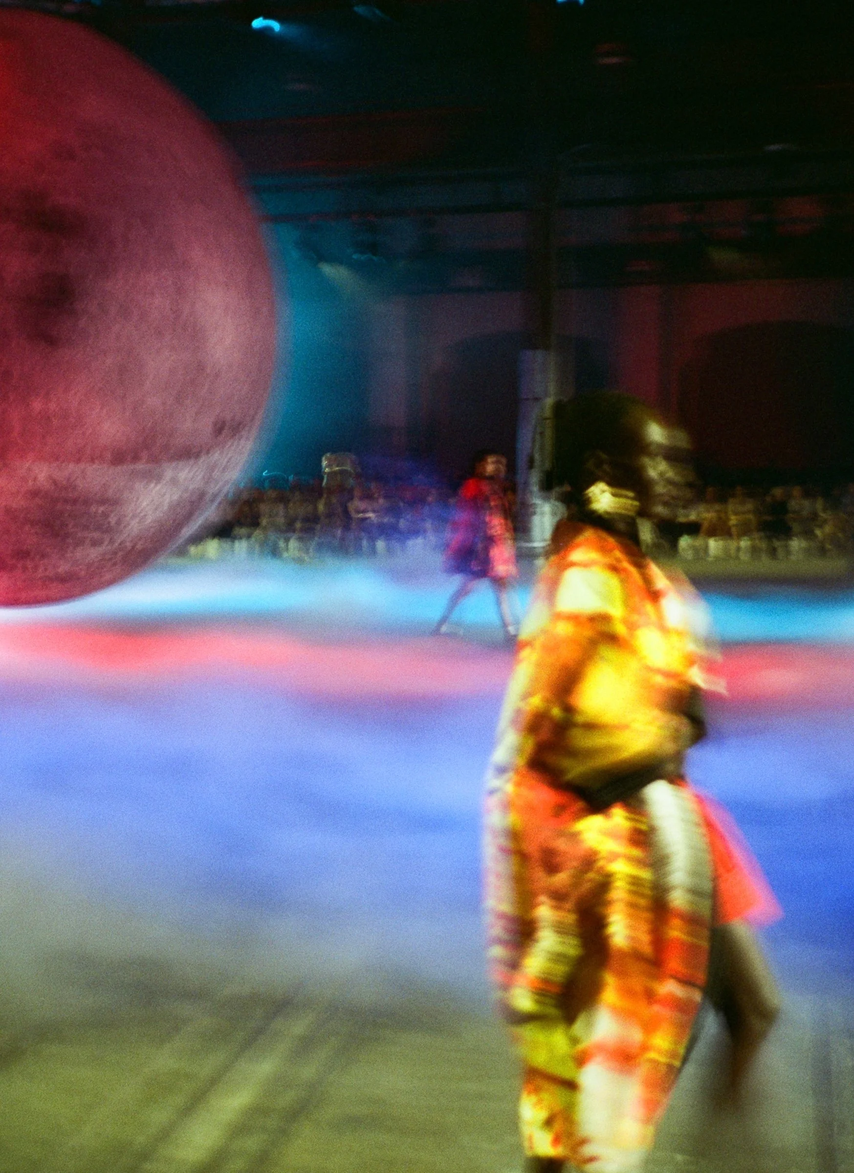 People in a colorful indoor roller skating rink with a large moon decoration and vibrant lighting.