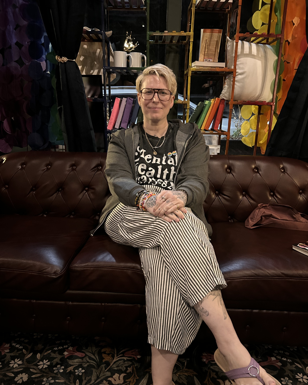Person sitting on a leather couch in a colorful room with bookshelves and patterned walls.