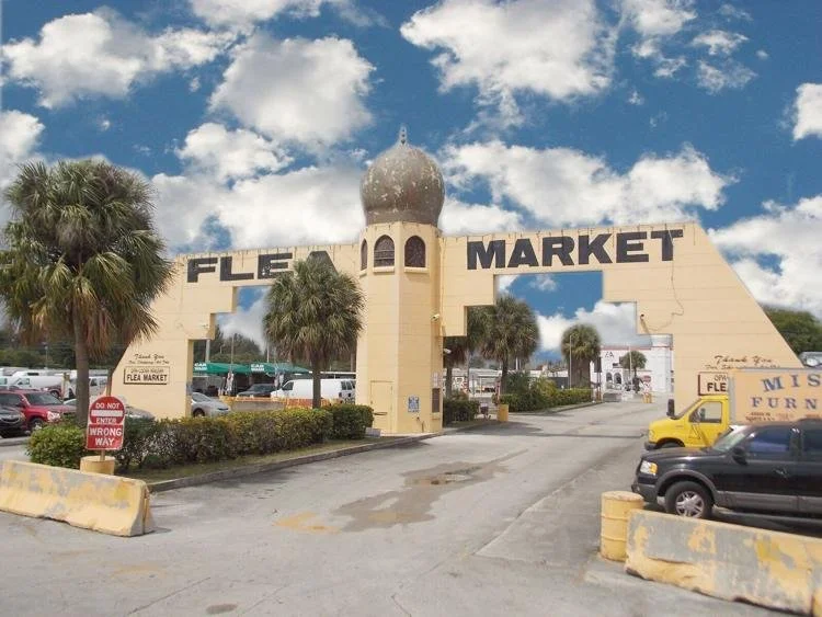 Entrance sign for Flea Market with a beige archway and a dome on top, surrounded by palm trees, parked cars, and cloudy sky.