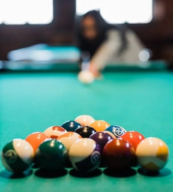 Pool balls arranged on a billiards table with a person preparing to take a shot in the background.