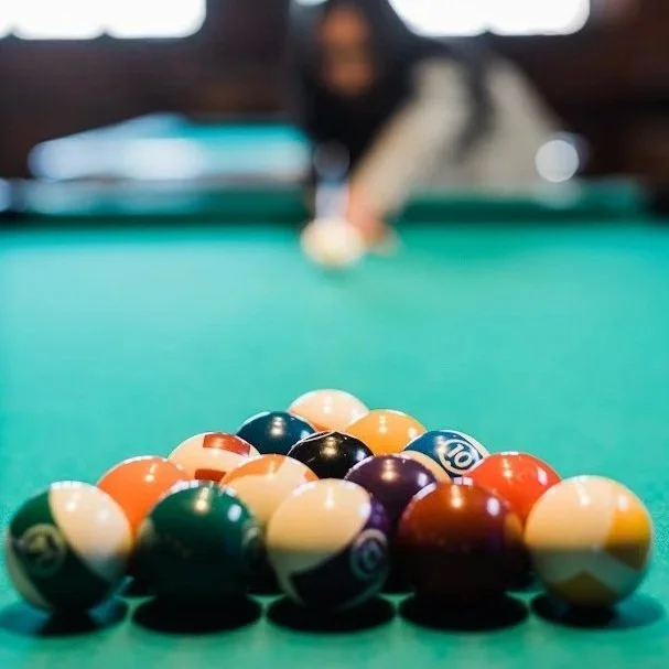 Pool balls arranged on a green billiard table with a person aiming at the cue ball in the background.