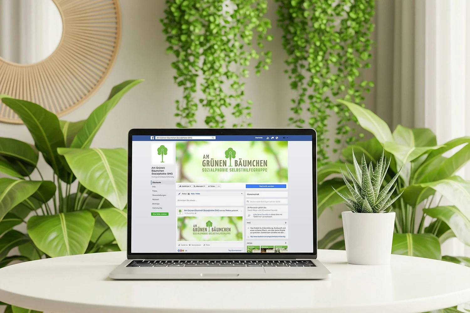 Laptop on a white table displaying a Facebook page for 'Am Grünen Bäumchen,' a social therapy self-help group, surrounded by green houseplants indoors.