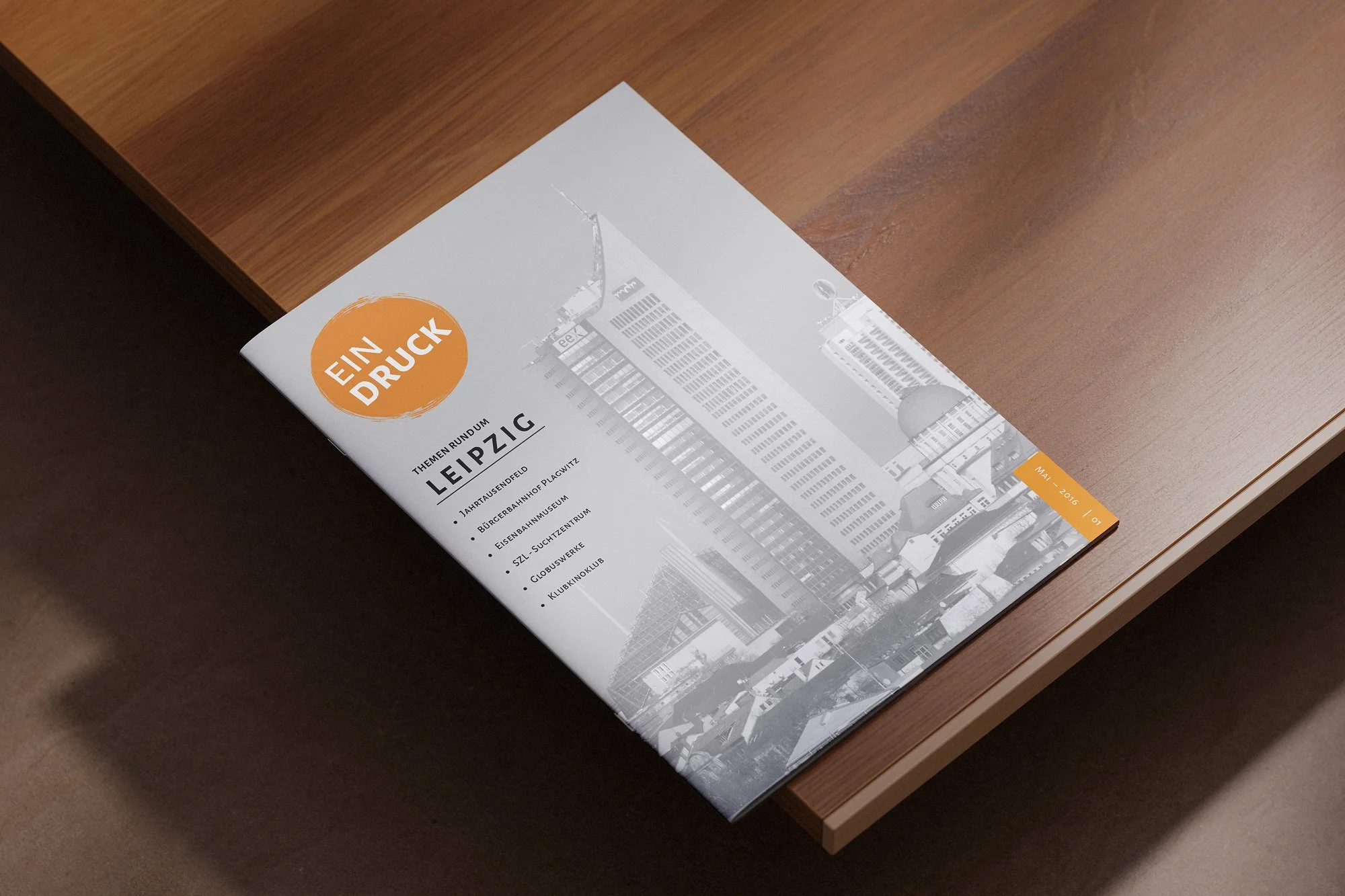 A magazine titled 'Ein Druck' with a cityscape cover, placed on a wooden surface, with a list of topics including Leipzig, and featuring a black and white photograph of buildings.