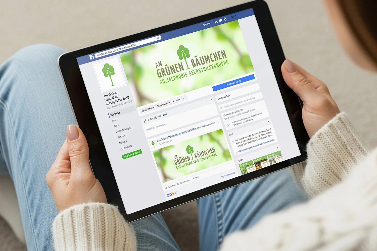 Person holding a tablet showing a Facebook page for a support group called 'Am Grünen Bäumchen,' featuring a logo with a green tree and a green background.