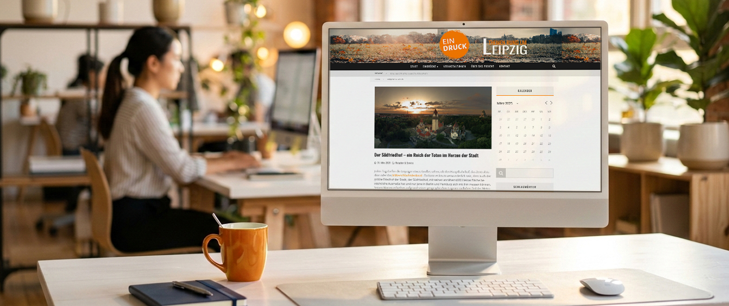 Computer on a desk showing a website in German about Leipzig, Germany, with a photo of a sunset over a church, in a busy office with a woman working at a computer in the background.