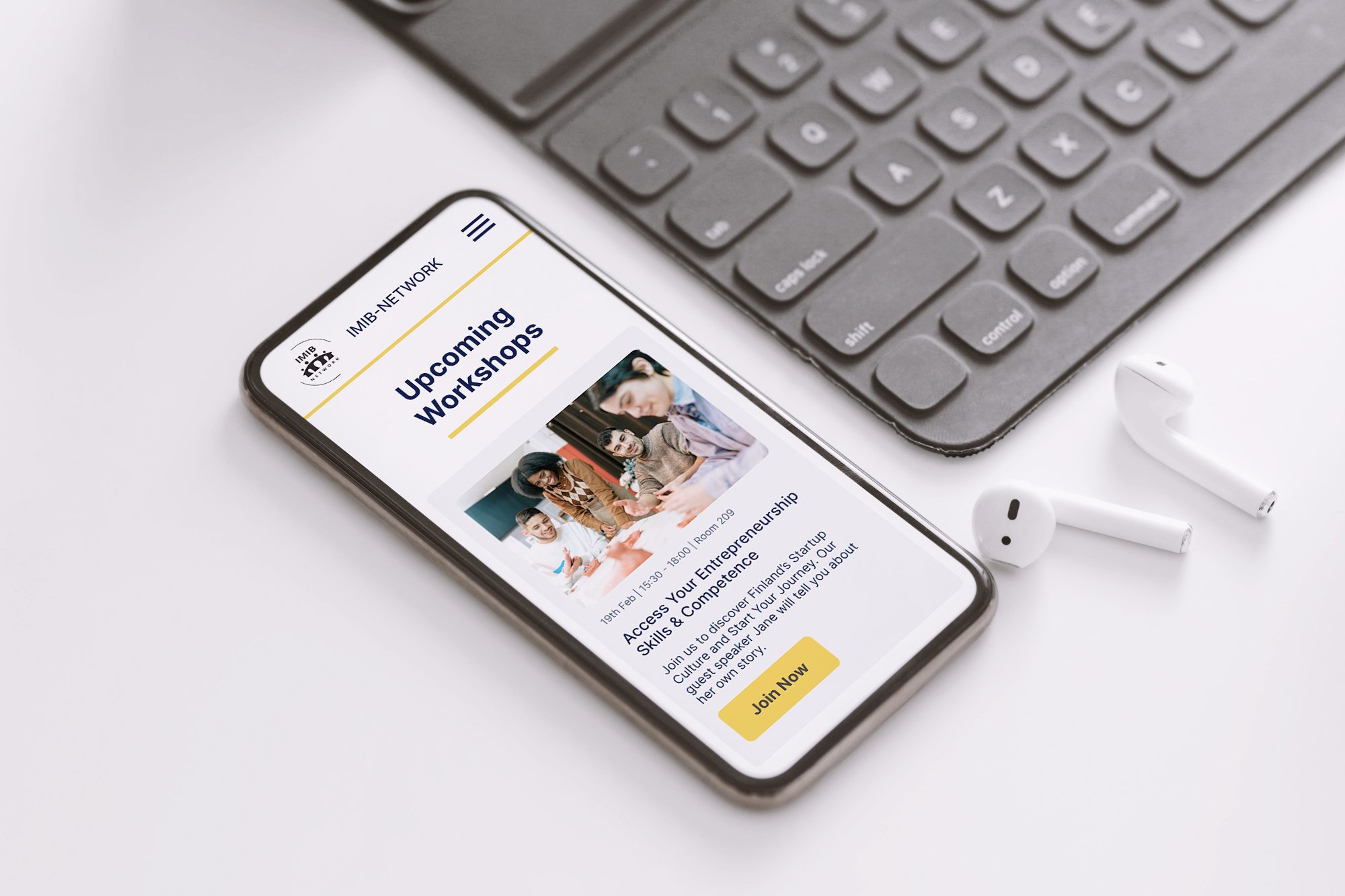 Smartphone displaying upcoming workshop on entrepreneurship with a 'Join Now' button, placed on a white surface near wireless earbuds and a black keyboard.