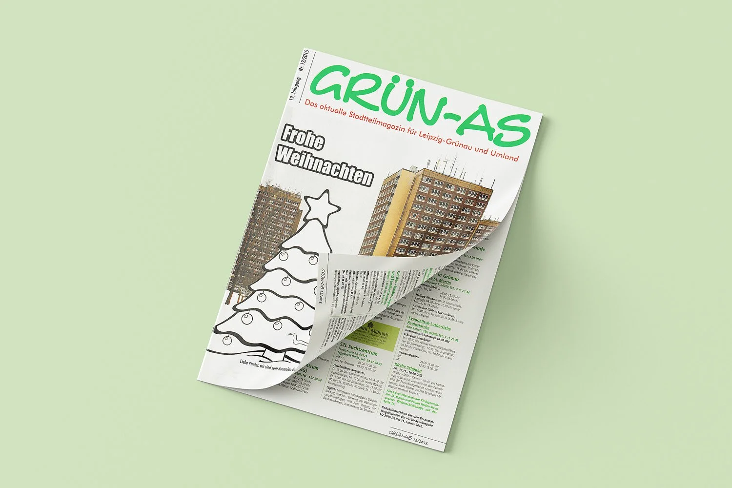 A folded newspaper titled 'GRÜN-AS' with Christmas-themed illustration and Christmas message, laid on a light green surface.
