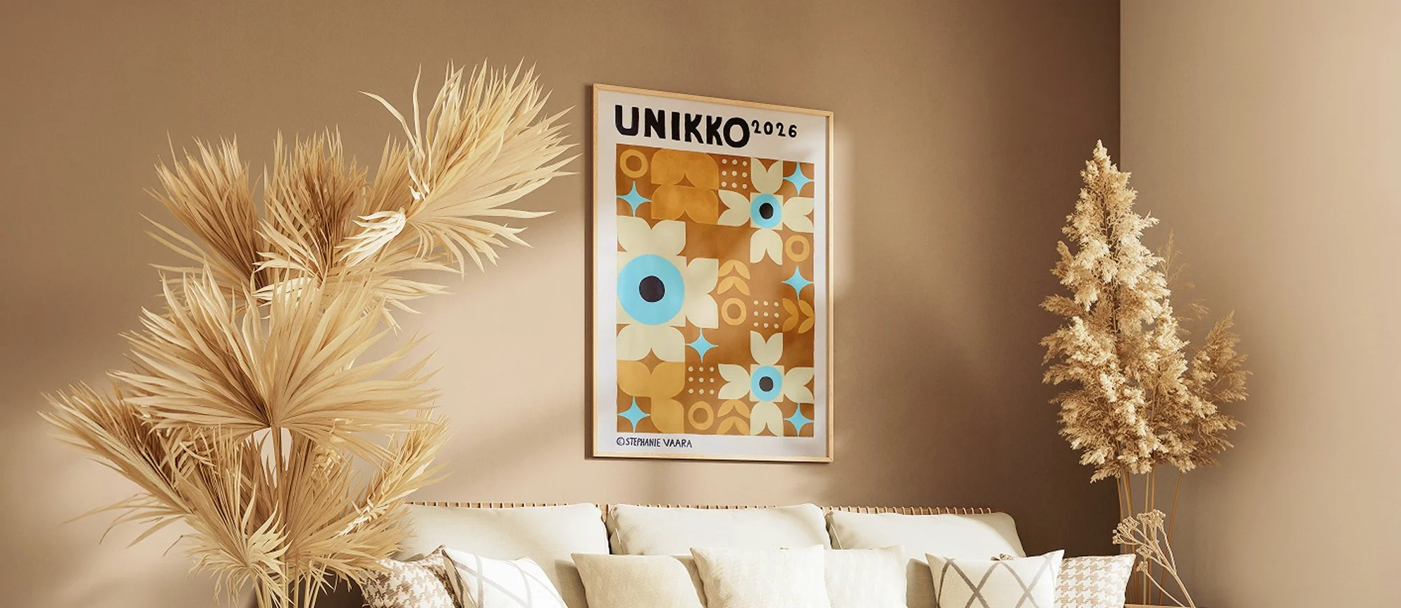 Decorative indoor scene with beige walls, a abstract modern art print with floral designs and text, beige pillows on a couch, and dried neutral-colored plants.