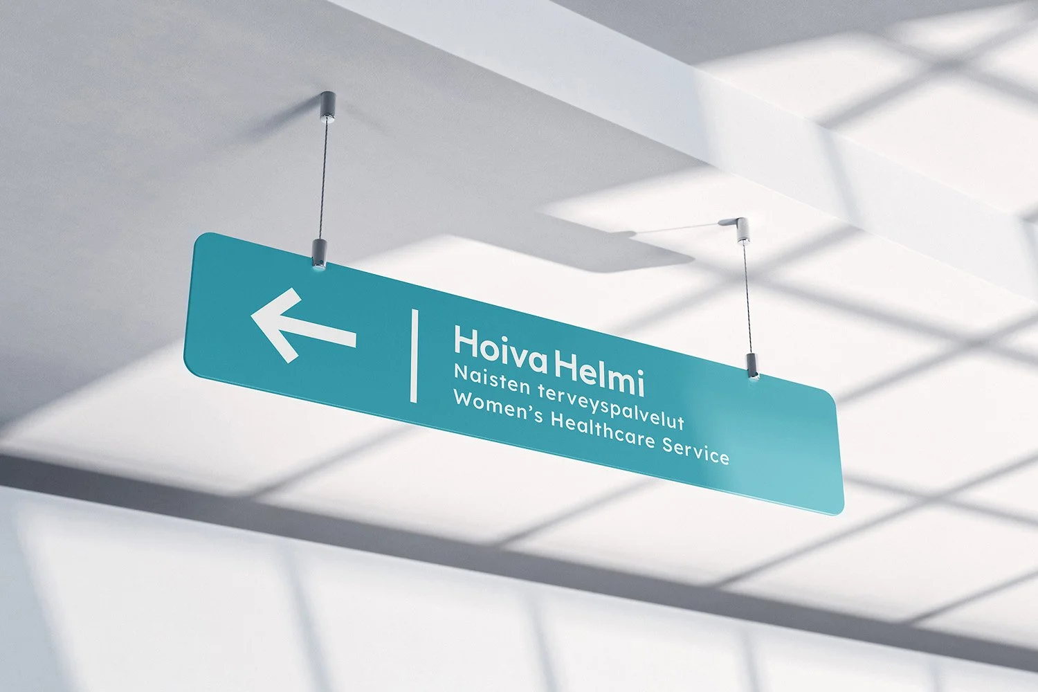 A blue directional sign hanging from the ceiling indicating the Women's Healthcare Service at Hoiva Helmi, with an arrow pointing to the left.