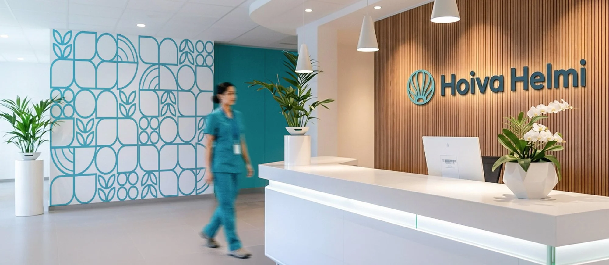 Reception area with a white counter, potted plants, and a wooden wall with the logo 'Hoiva Helmi' in blue. A blurred nurse in blue scrubs walks past.
