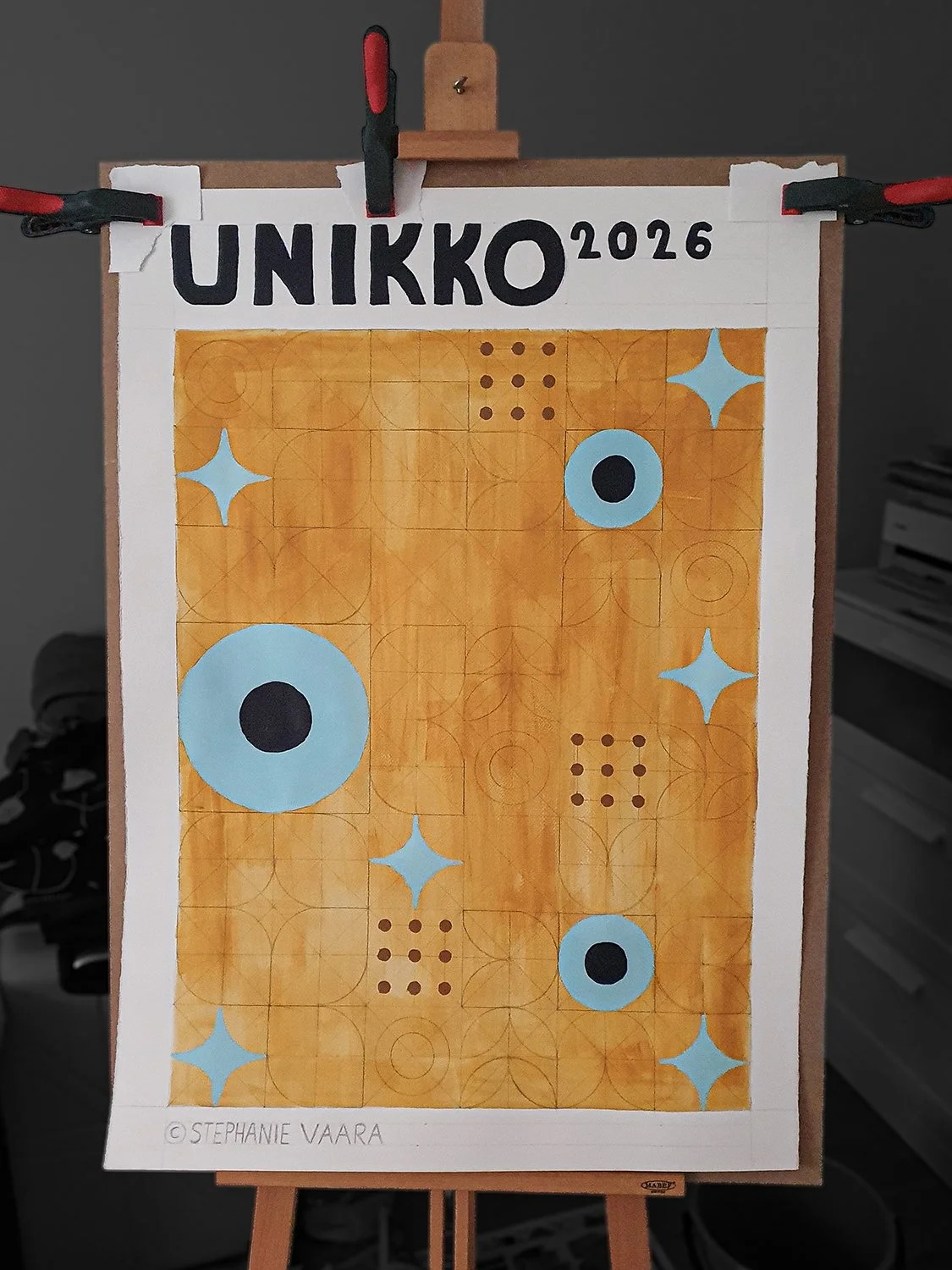 Artwork titled UNIKKO 2026 by Stephanie Vaara featuring colorful geometric shapes and patterns on an orange background, displayed on an easel.
