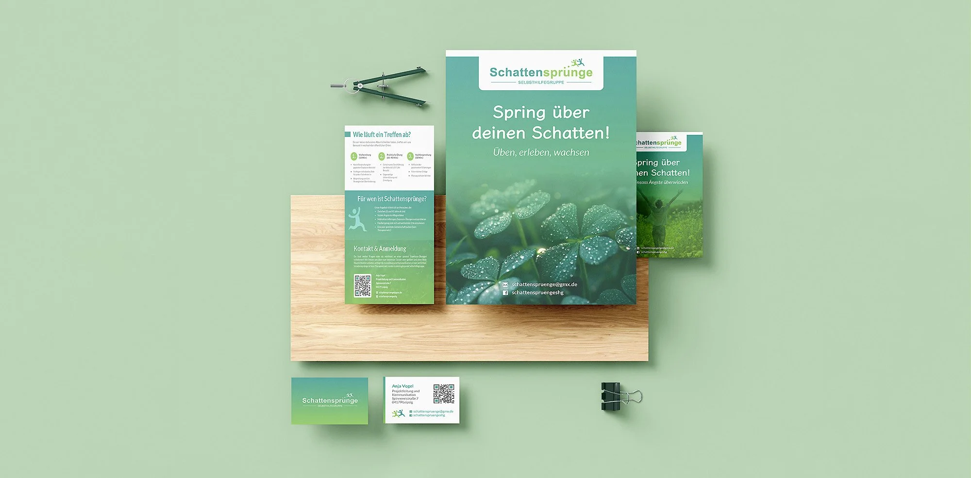 Brochure and flyers with green themes and water droplets images on a wooden desk, along with a black binder clip and business card for Schatten Sprünge, a self-help group.