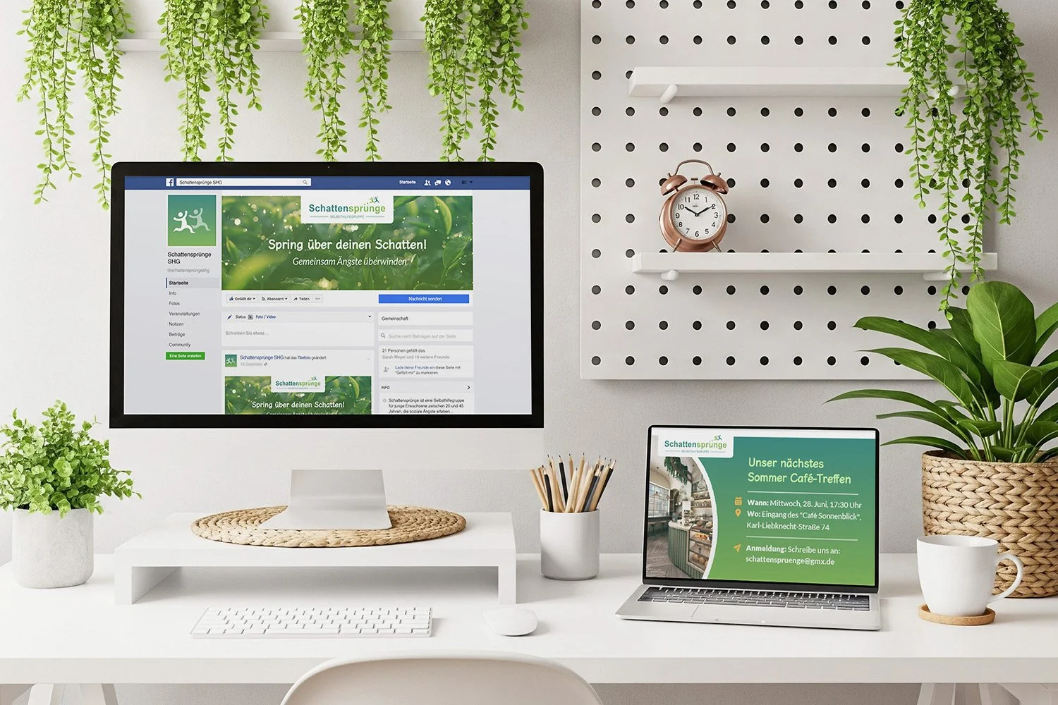 A modern white desk with a large computer monitor and a smaller laptop, both displaying social media and event information for a group called Schatten Sprünge. The desk has potted plants, a white keyboard, and a mouse. A wall with decorative hanging 
