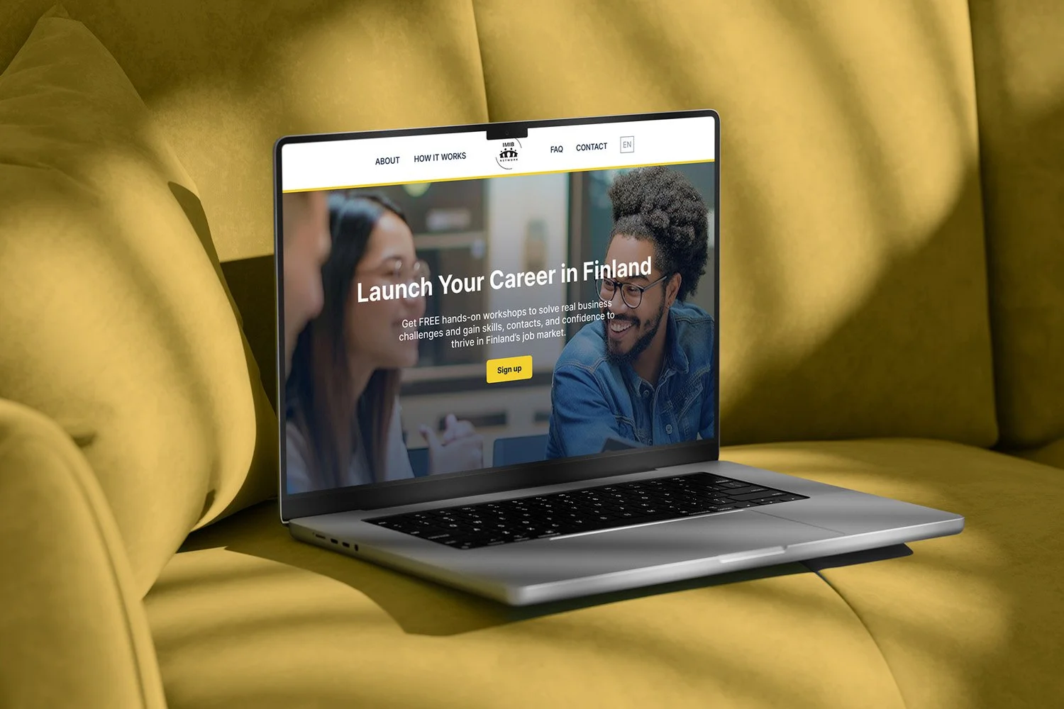 Laptop on yellow couch displaying a website with the heading 'Launch Your Career in Finland' and a yellow 'Sign up' button, featuring an image of smiling young adults.