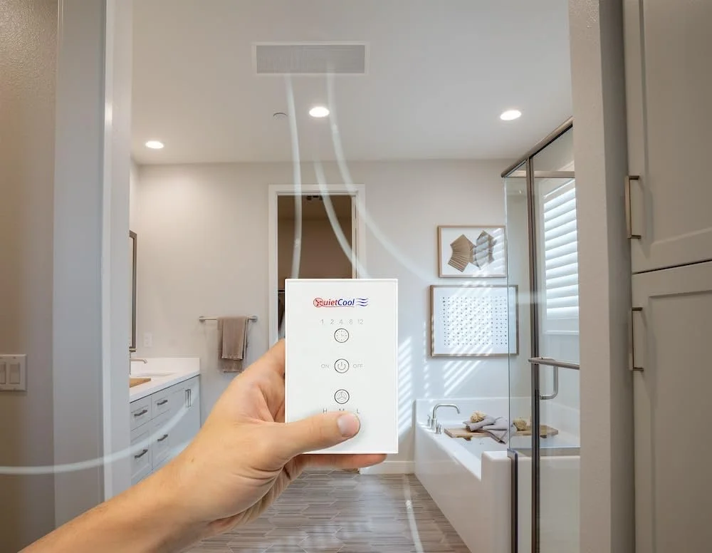 Person holding a remote control for a bathroom infrared heater, projecting heat rays in a modern bathroom with a bathtub, shower, and window. QuietCool Whole House Fan San Diego