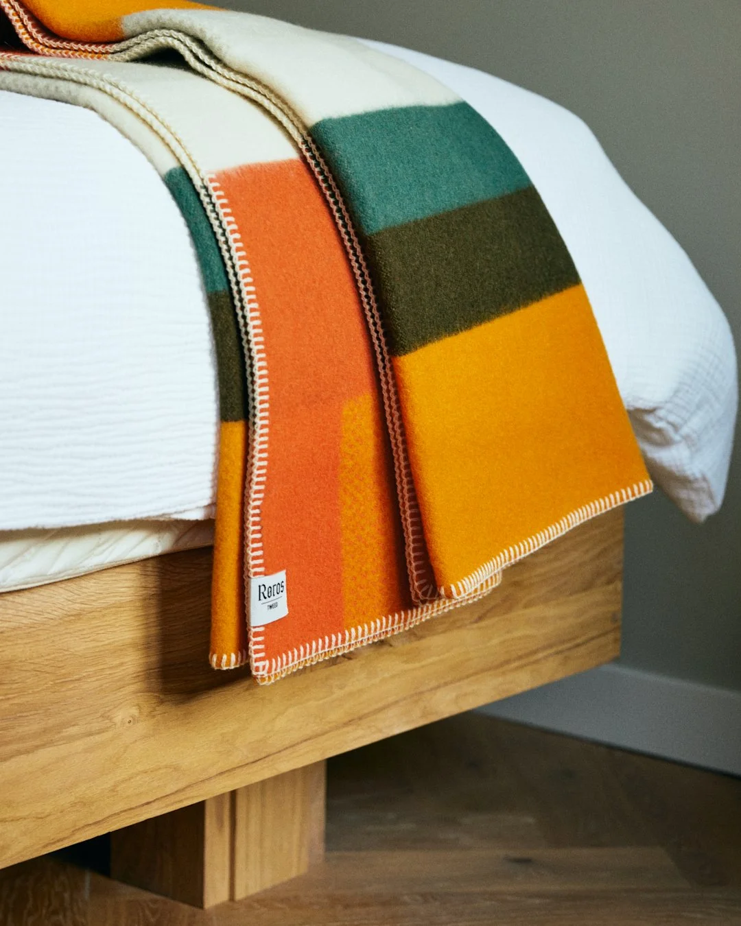 Close-up of a colorful striped blanket draped over a beautifully crafted custom bed frame with cocomatt mattresses and white duvet
