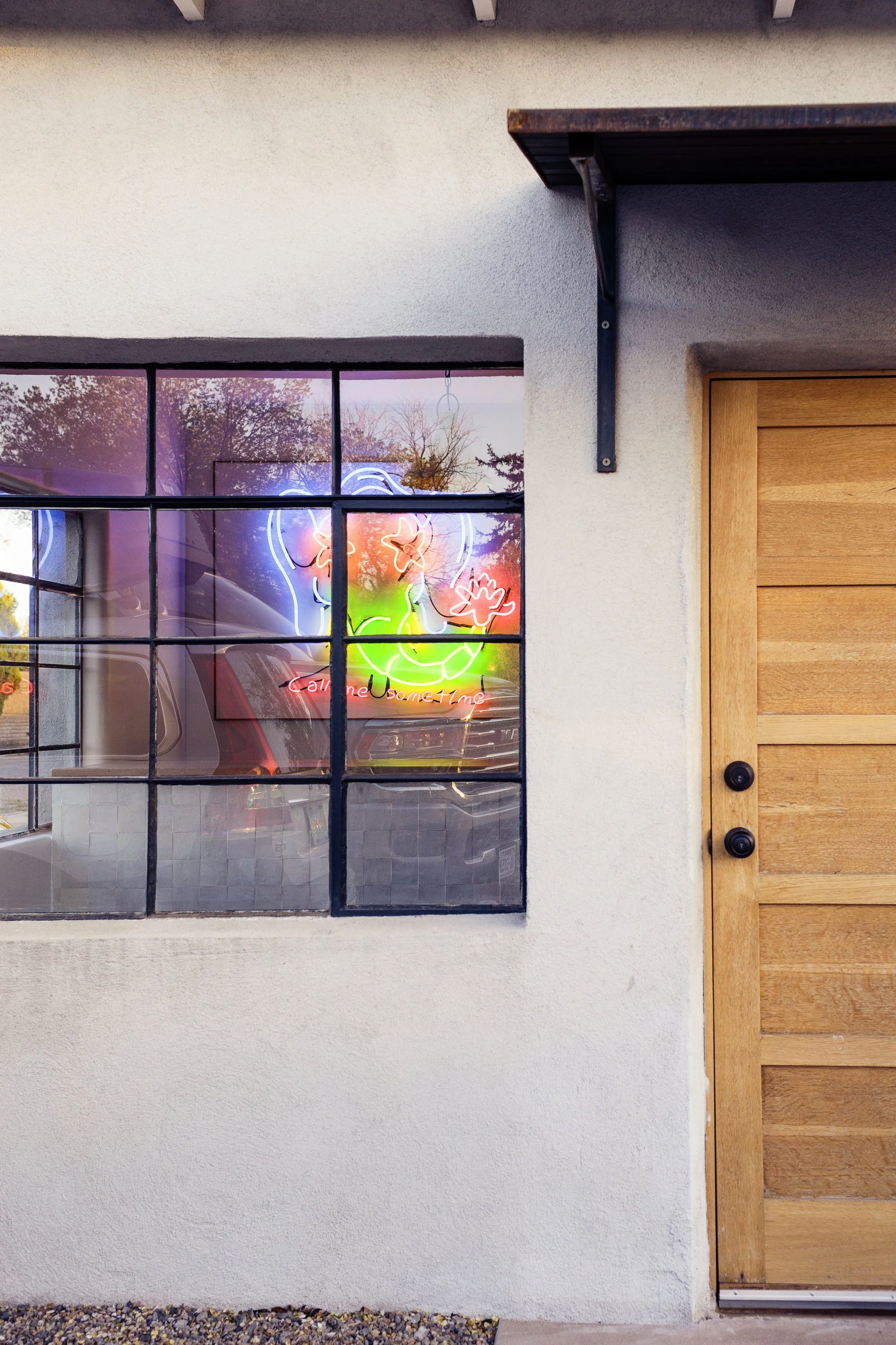 Close-up of a house window and wooden door, with a neon sign of a clown face and colorful lights visible through the window.