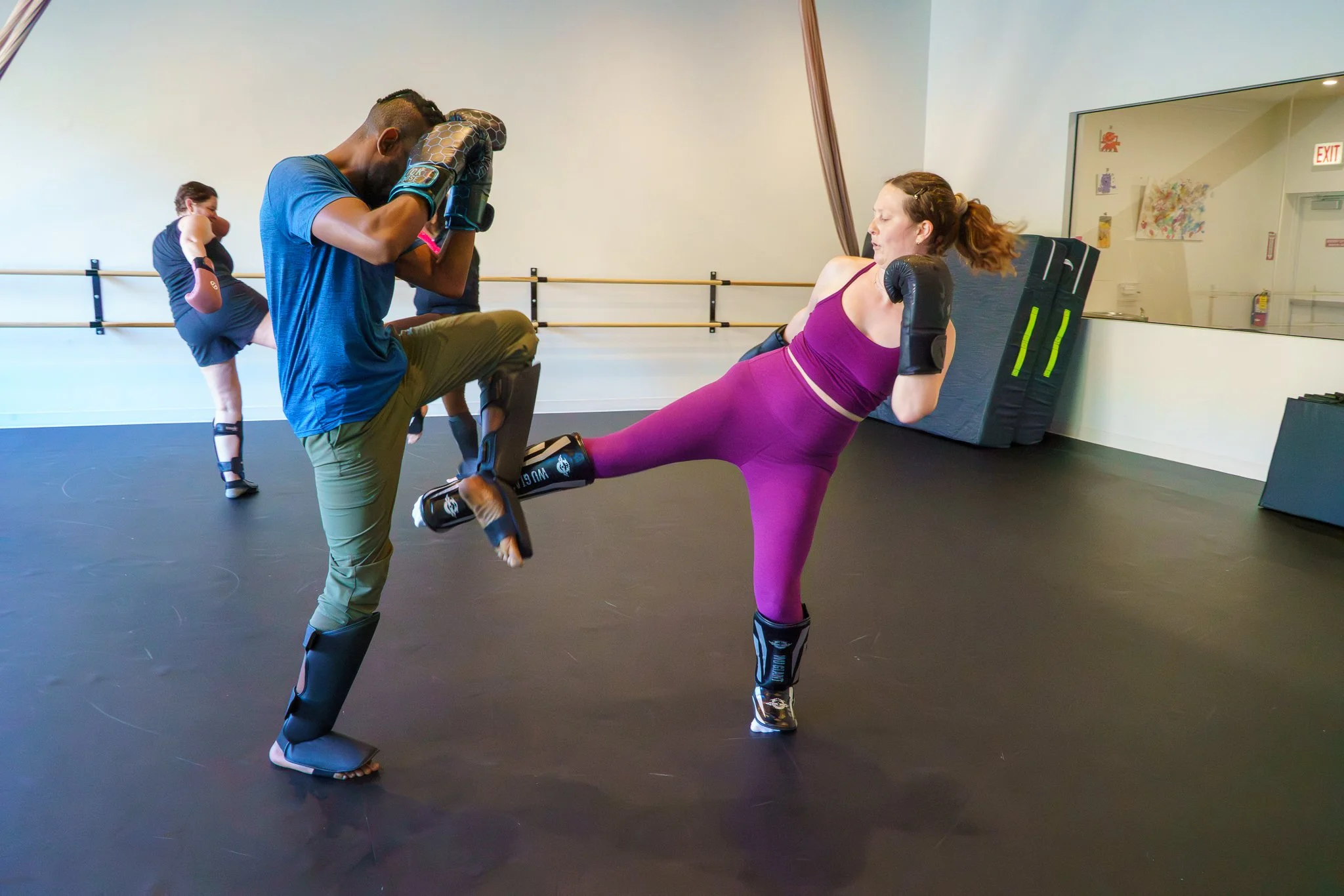 Female student throwing a lowkick and Coach AD checking that kick with their outside leg