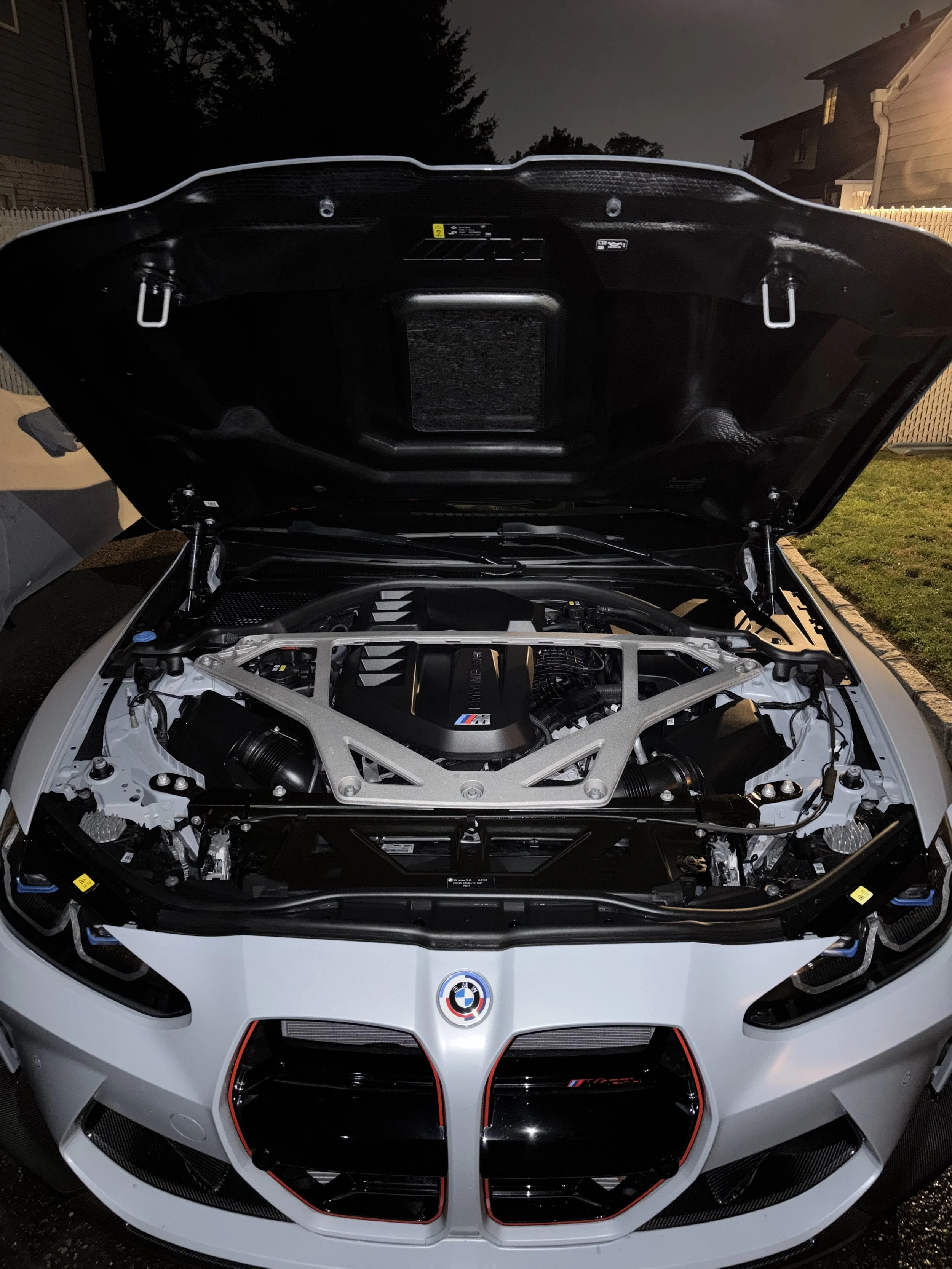 Front view of an open hood BMW M series car engine with visible engine components and BMW emblem.
