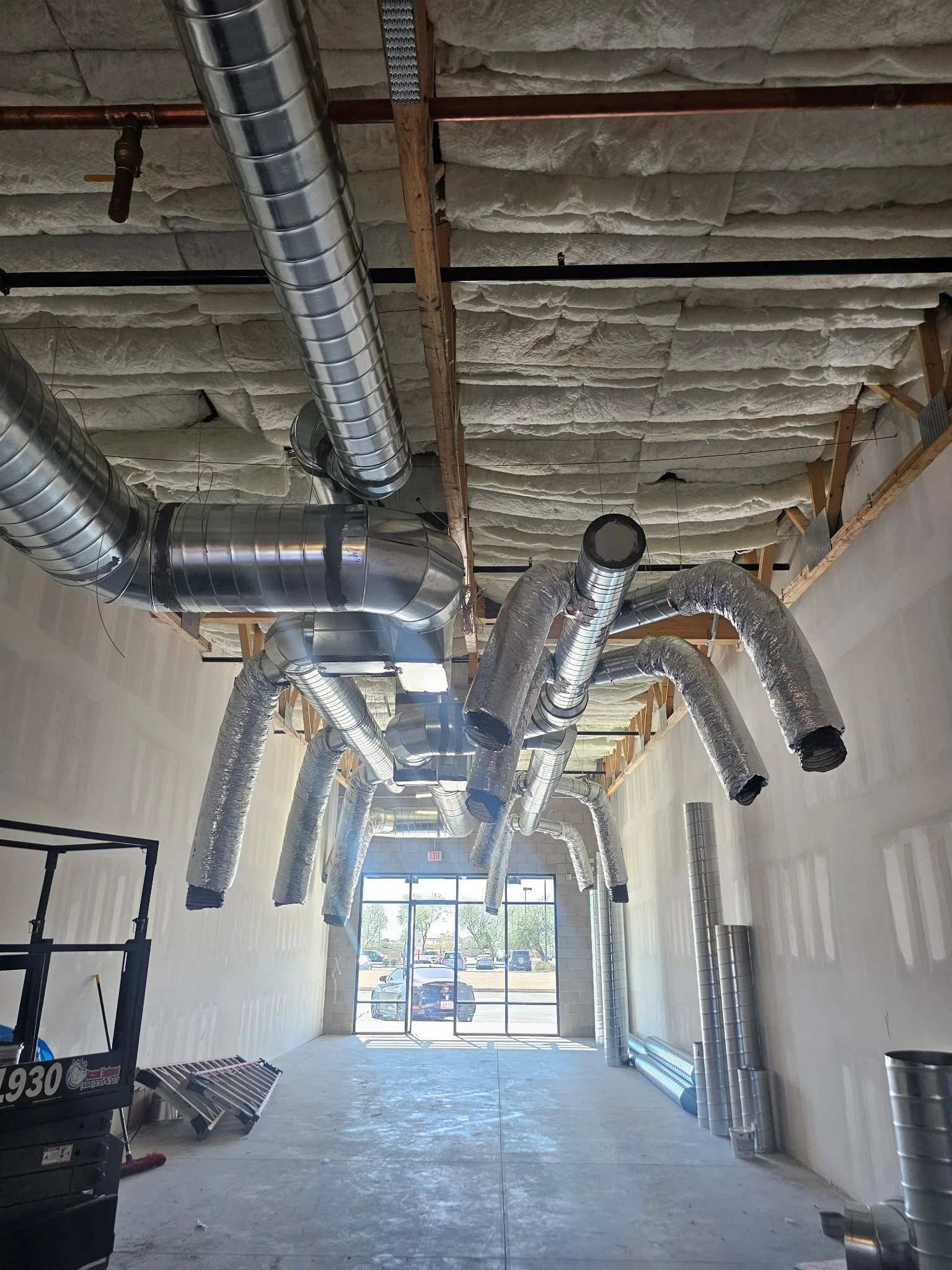 Construction site interior with exposed ductwork and insulation on the ceiling, and a large window at the front.
