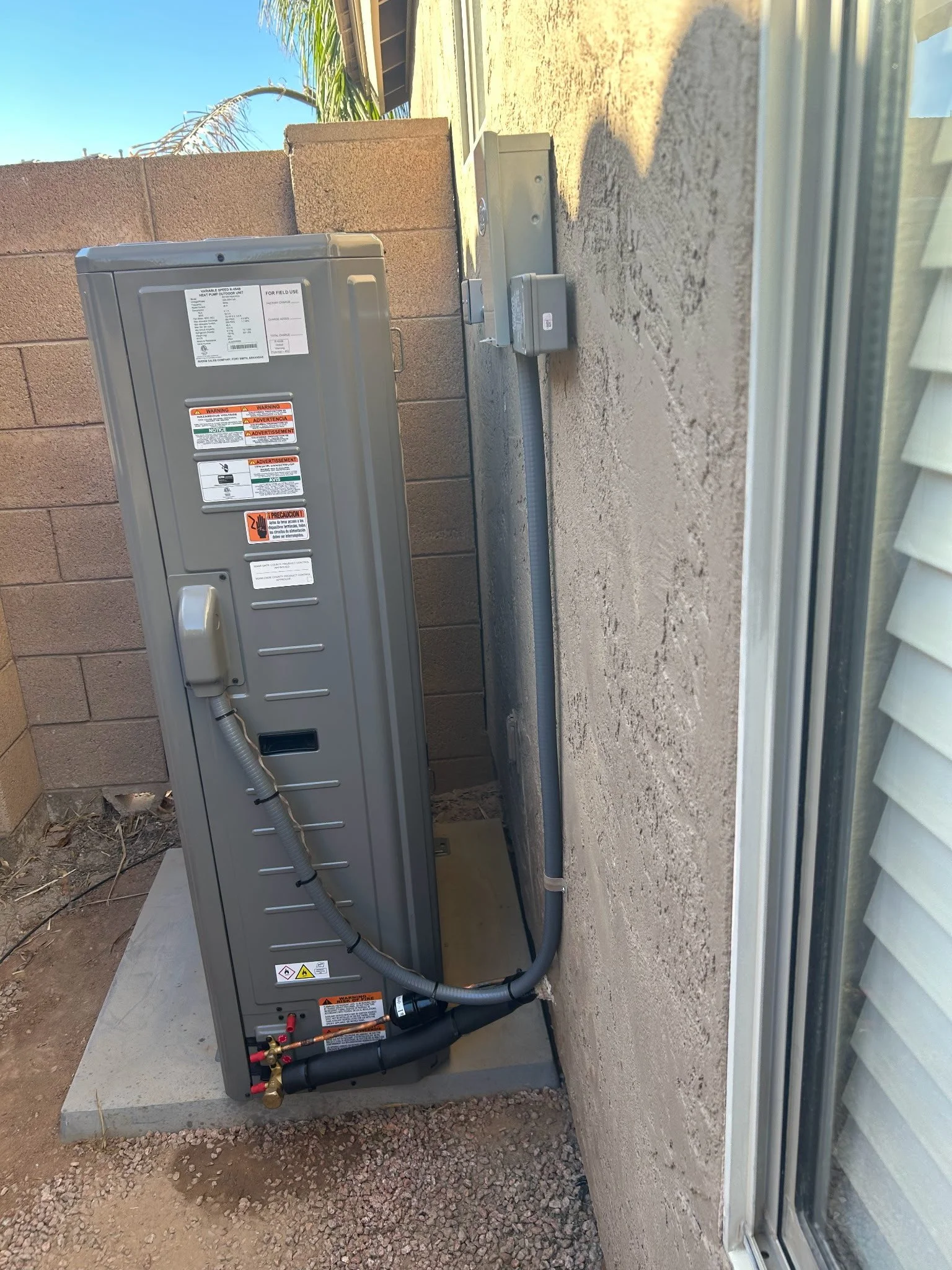 Outdoor electrical panel and utility box mounted on a wall next to a window, with exposed wiring and warning labels.