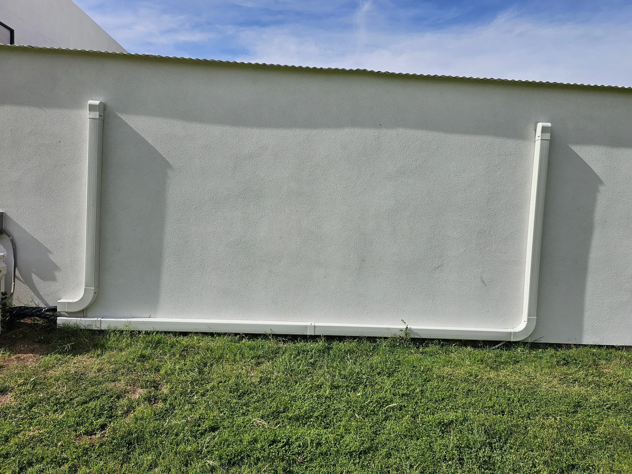 Exterior white wall of a building with decorative pipes and grass in the foreground.