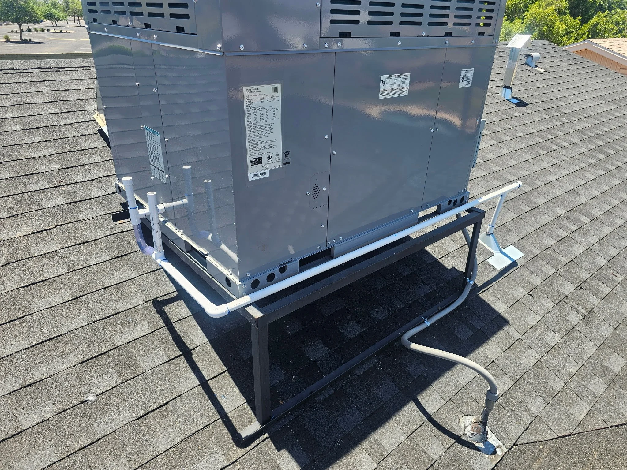A rooftop HVAC unit with pipes and a black metal frame on a shingled roof.