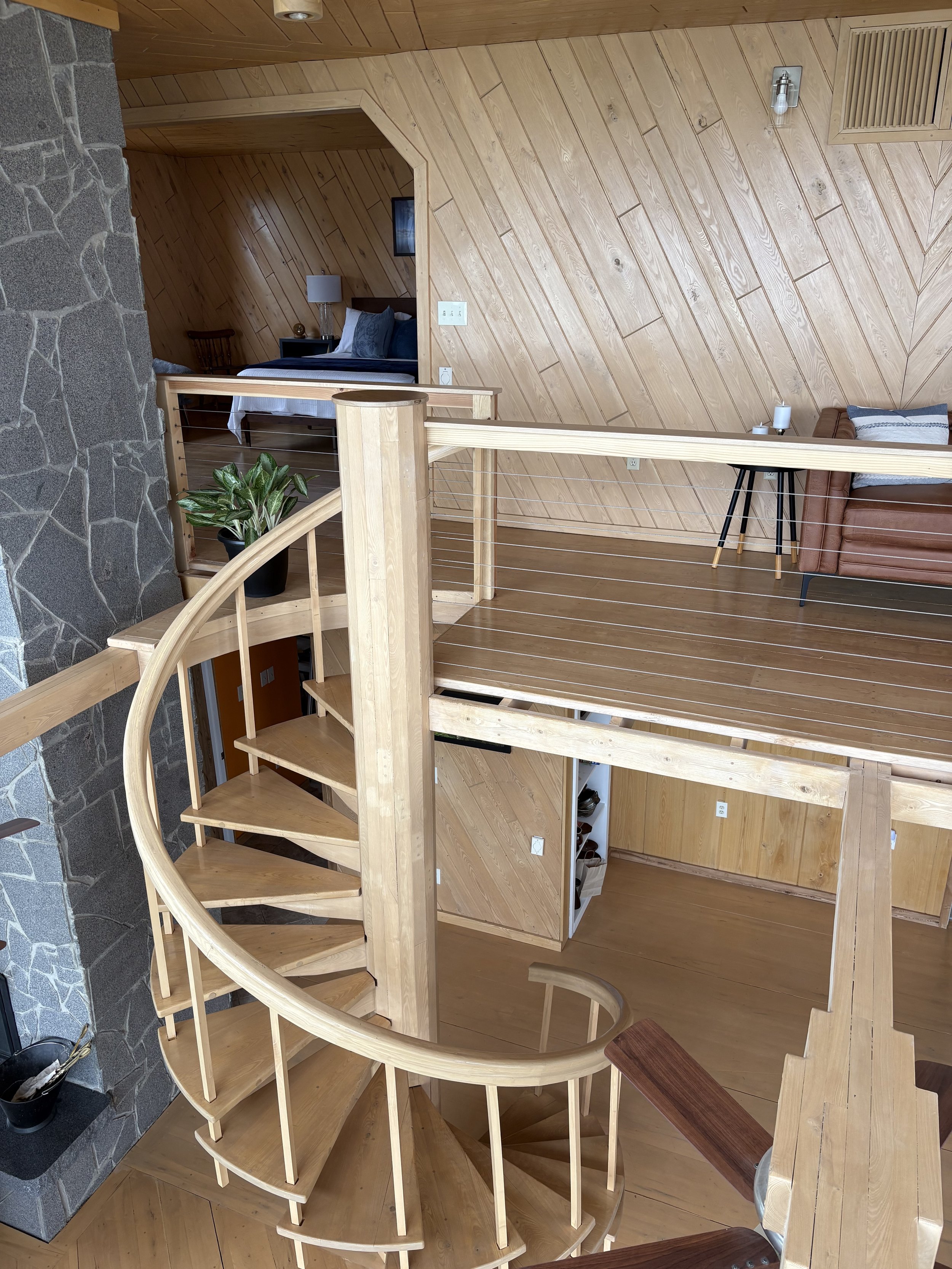 Interior view of a multi-level wooden staircase overlooking a living area with wooden walls and a sitting area with a leather sofa, side table, and decorative items.