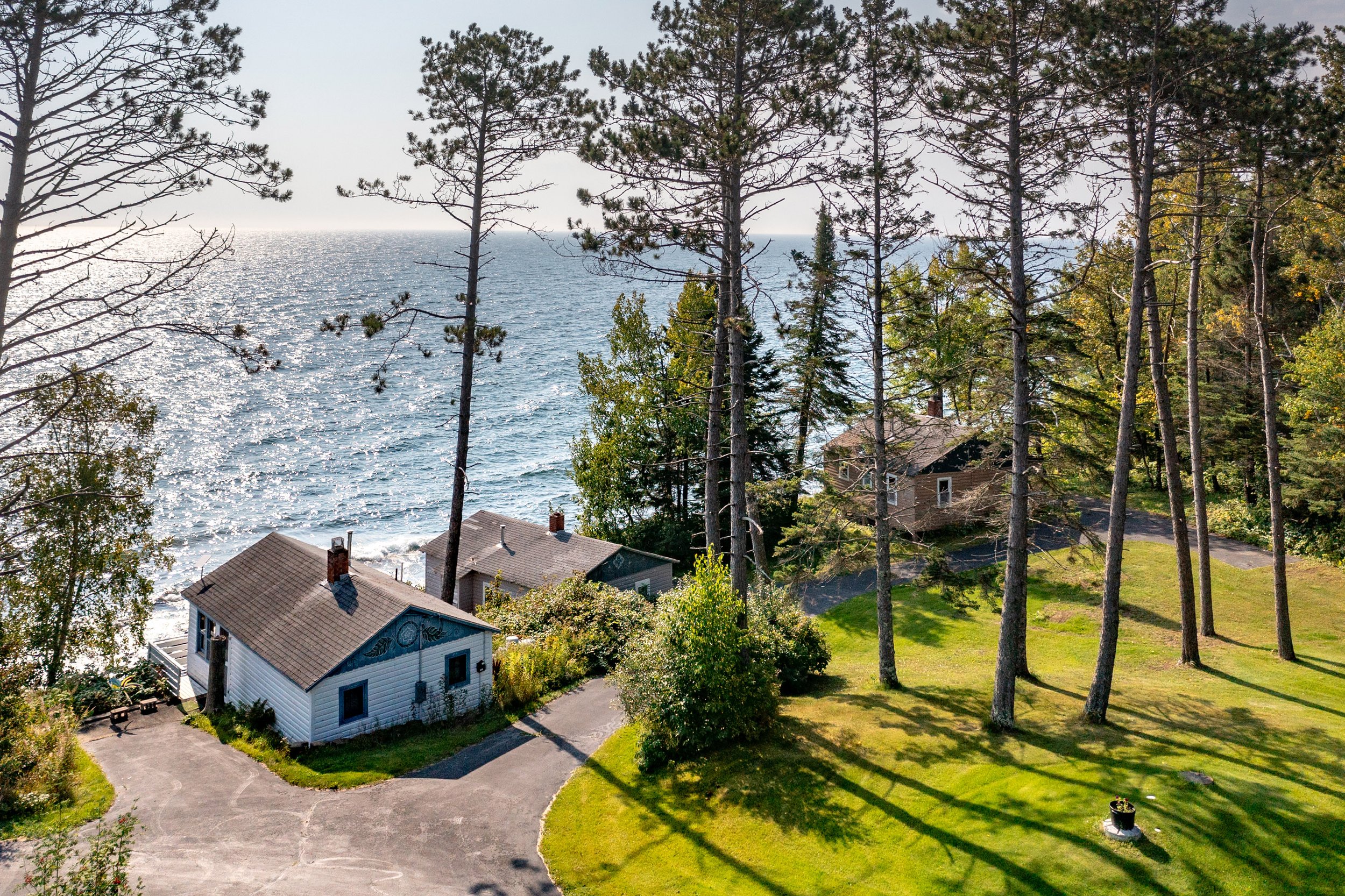 Houses by a lake with trees and a green yard, sunlight reflecting on the water, and a clear sky.