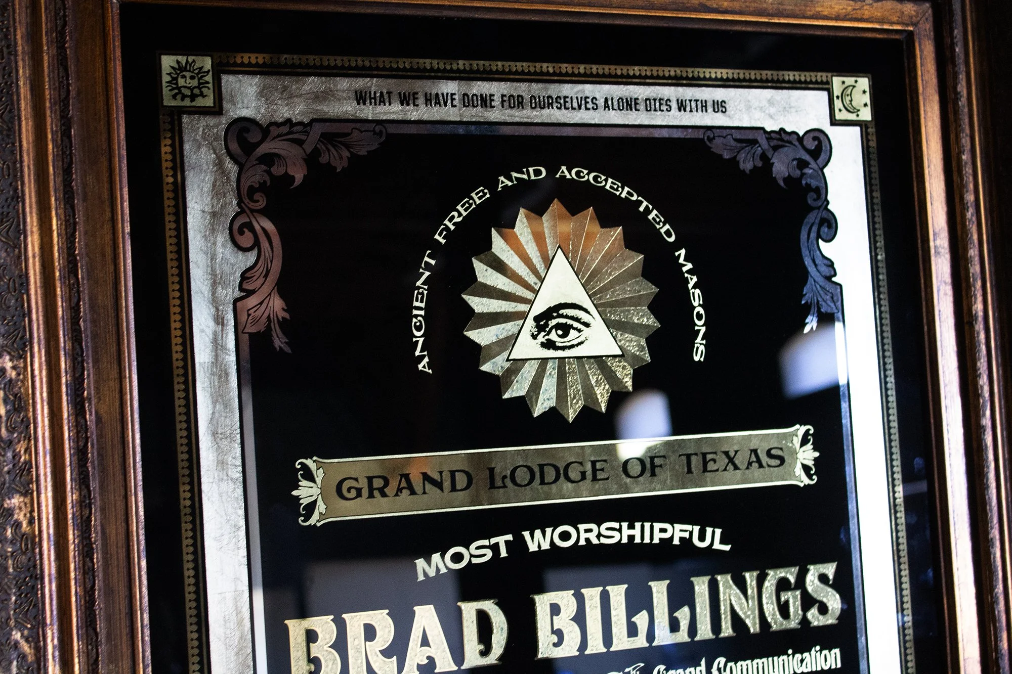 A framed decorative plaque with the logo of the Grand Lodge of Texas, featuring a triangle with an eye inside, surrounded by the phrase "Ancient Free and Accepted Masons." The plaque also reads "Most Worshipful Brad Billings" and "Grand Lodge of Texa