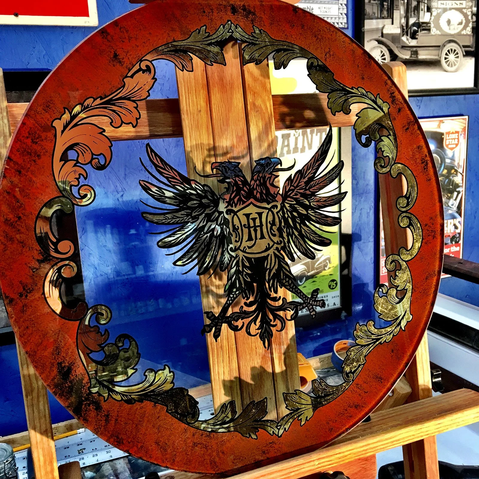 Glass Scottish Rite sign featuring an eagle with outstretched wings and holding a shield with the letter 'H' in the center, surrounded by ornate gold-colored scrollwork, framed in wood.