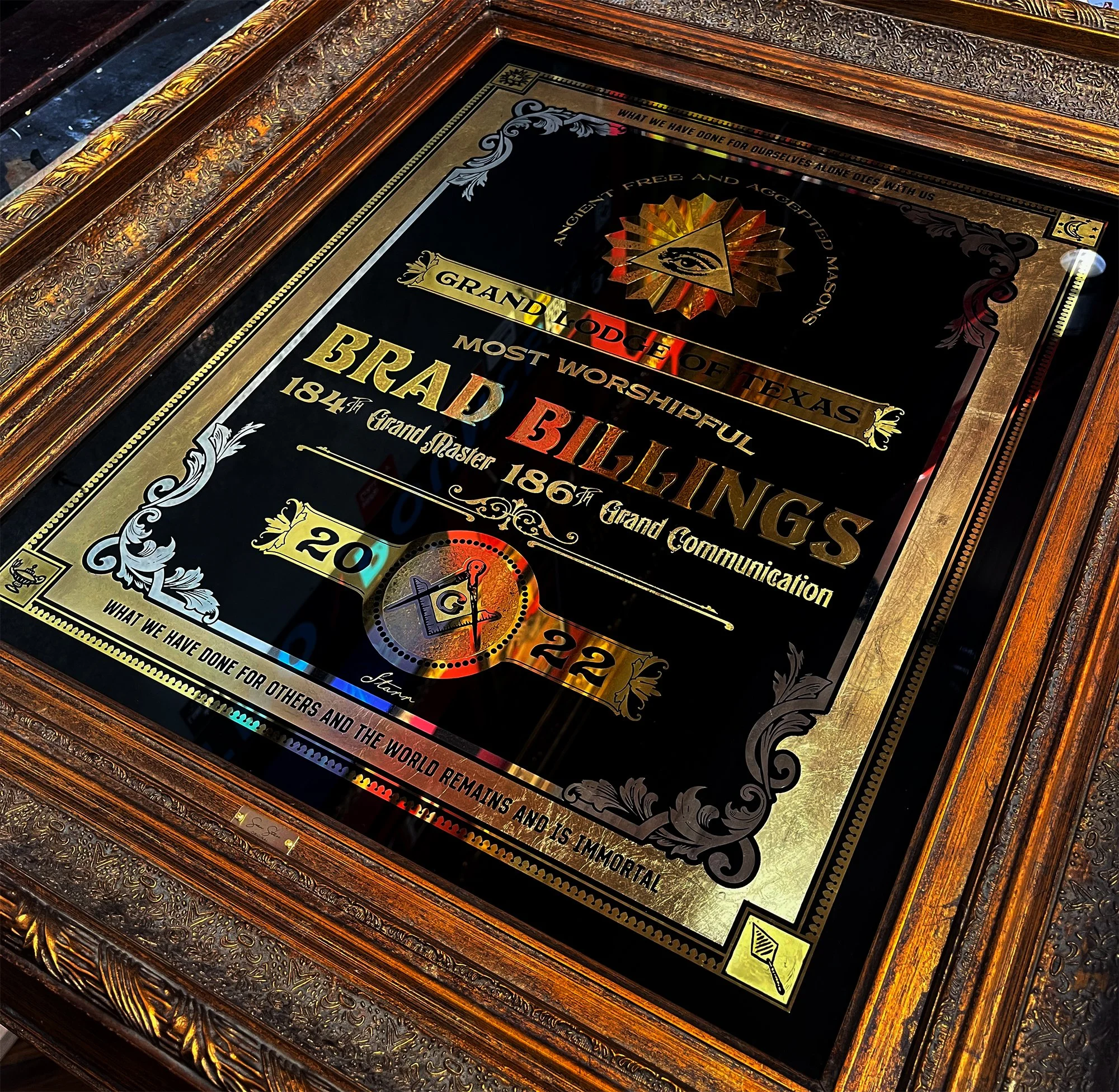 A framed plaque with ornate gold and silver details, honoring the Grand Lodge of Texas for the most worshipful Book of Bibles, referencing 1841, 1861, and 2022, with a symbol of an eye inside a pyramid, and decorative text celebrating Masonic achieve