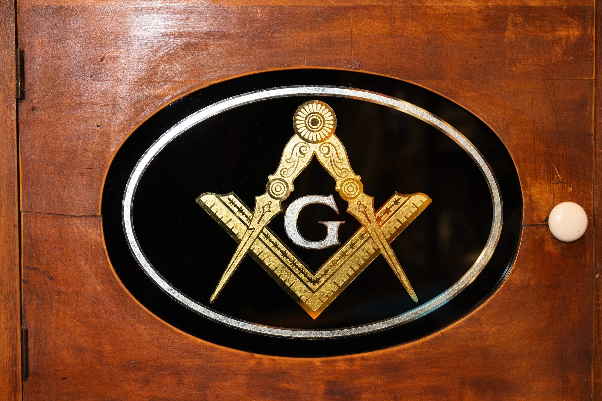 Freemason emblem with compass, square, and letter G inside an oval on a wooden background.
