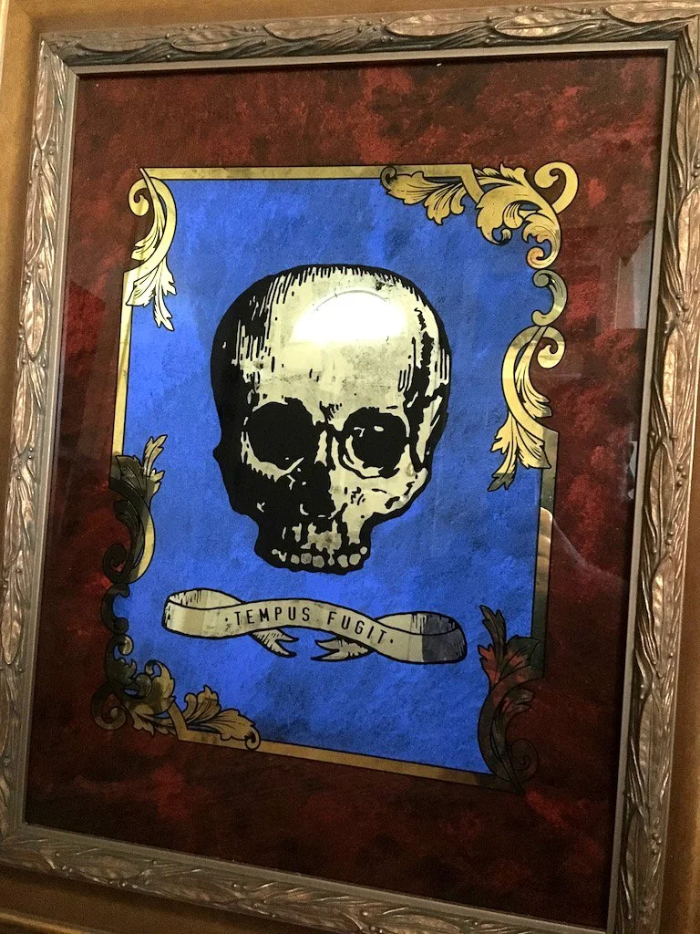 A framed artwork depicting a human skull on a blue background with gold and black decorative accents, and a banner below it reading "TEMPUS FUGIT."