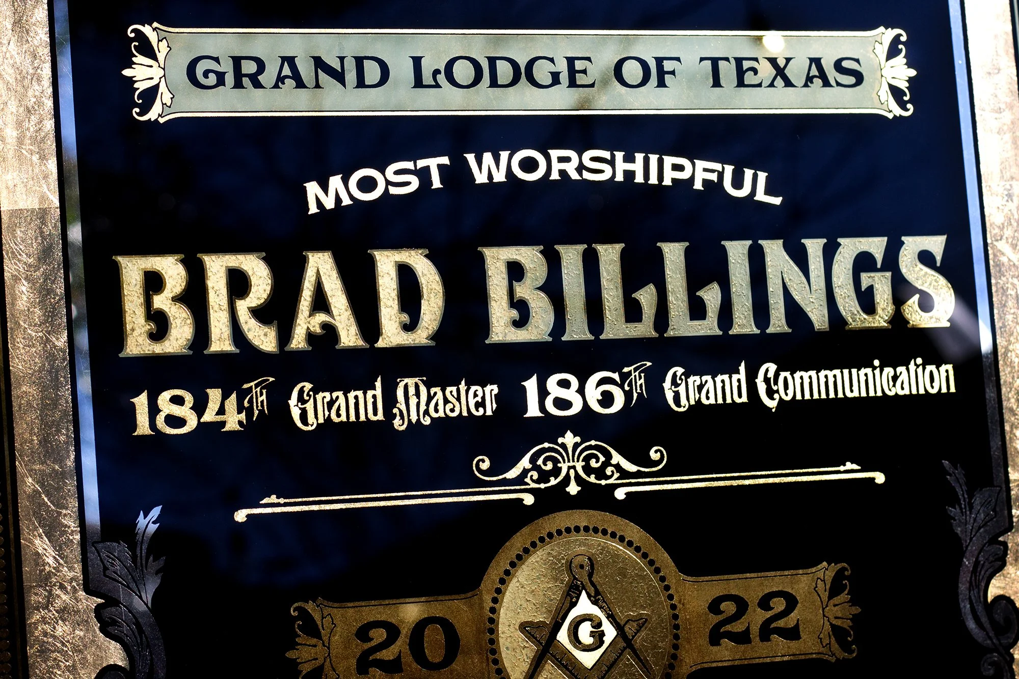 A black and gold sign for the Grand Lodge of Texas, indicating it is the most worshipful grand lodge, established in 1844 with a grand master in 1865, featuring decorative borders, text styles, and a Masonic symbol with a compass and square, and the 