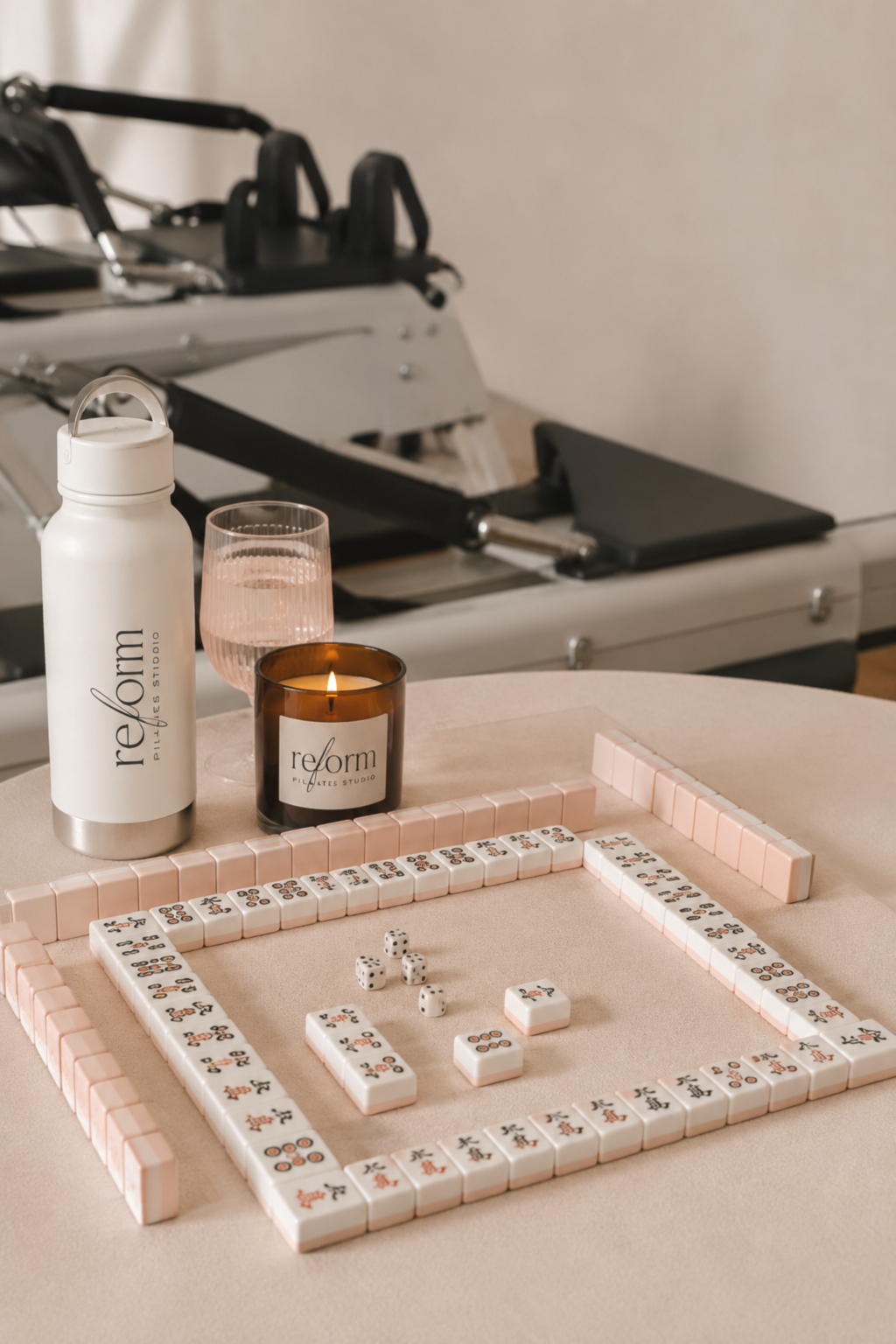 A mahjong table with a game set up. Drinks on the side with a REform candle along with a pilates reformer in the background.