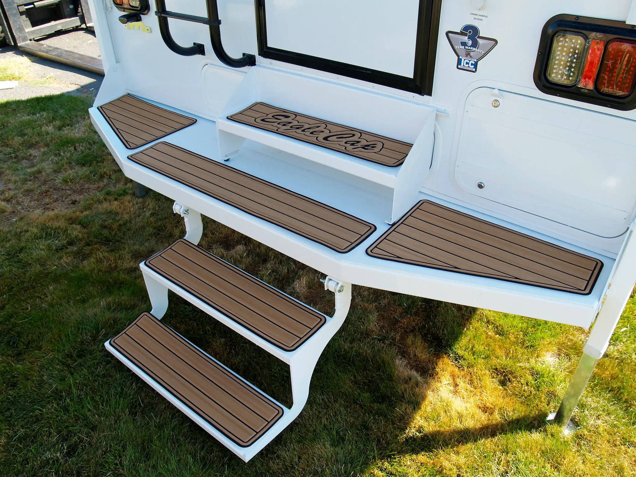 White RV exterior with a set of brown and black rubber mats on the steps and a small bench marked with the words "Eat Sleep".