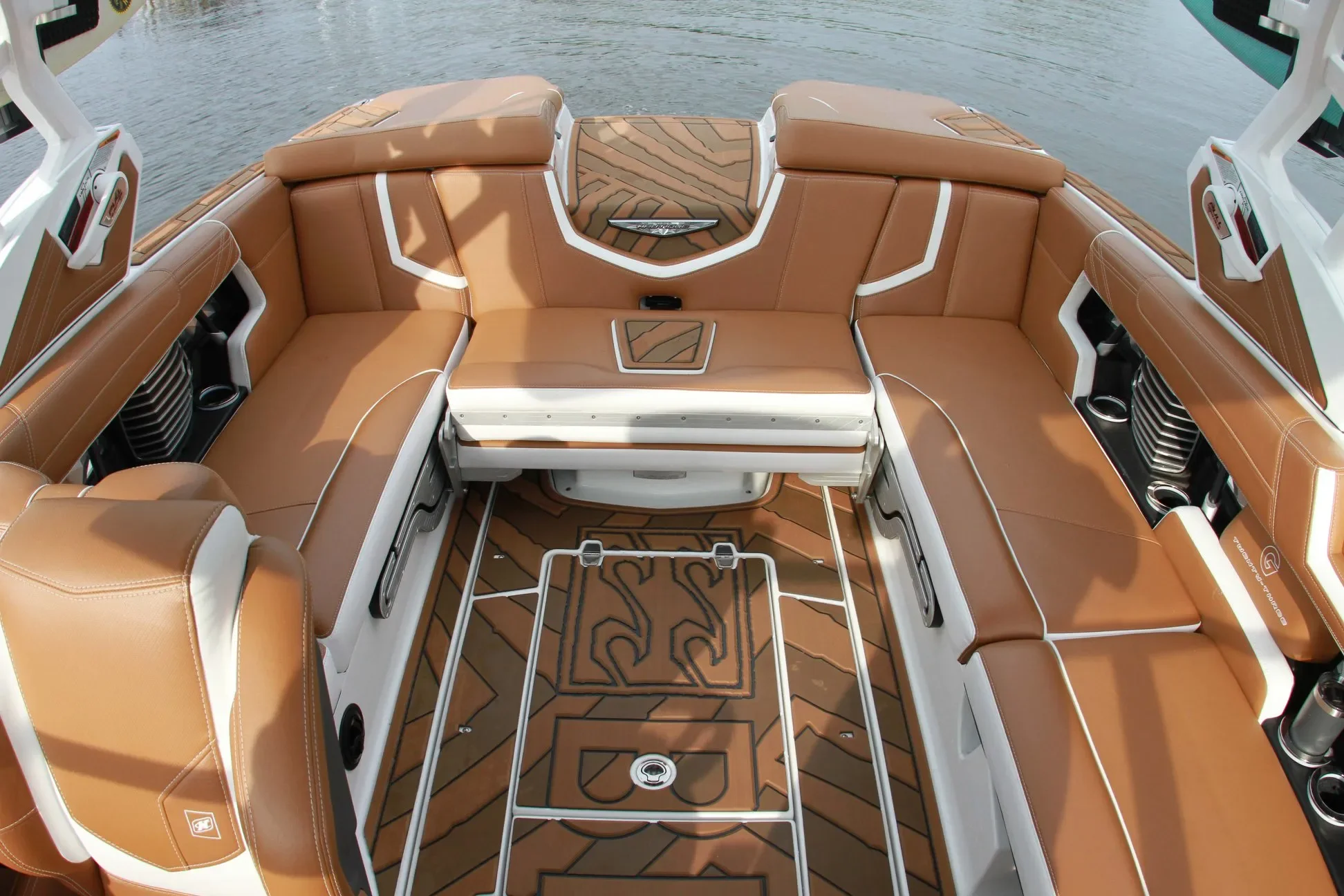 View of the interior seating area of a luxury boat with tan cushioned seats, white trim, and a patterned wood floor, with water visible in the background.