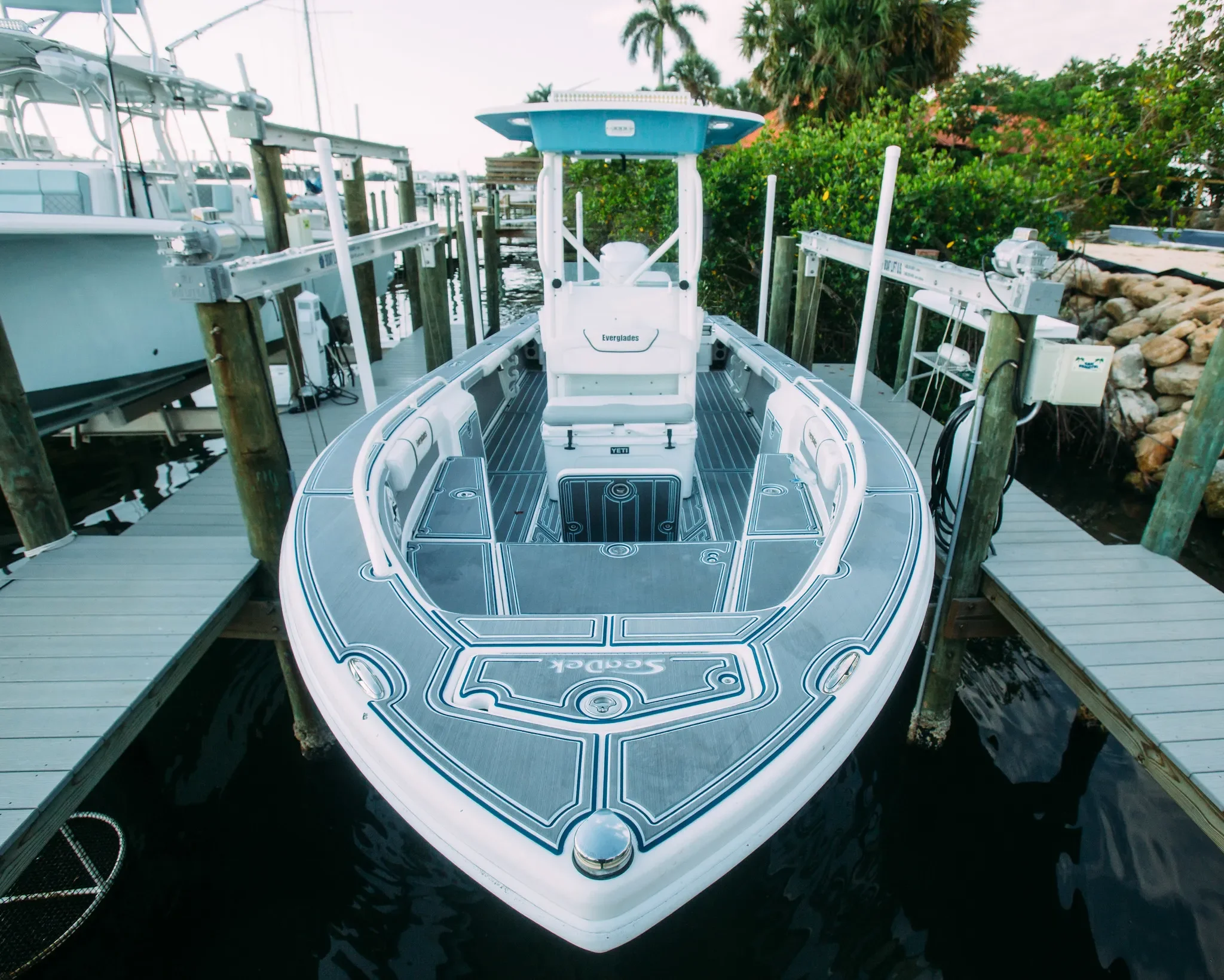 A sleek, modern boat docked at a marina, surrounded by wooden piers and lush green trees in the background.