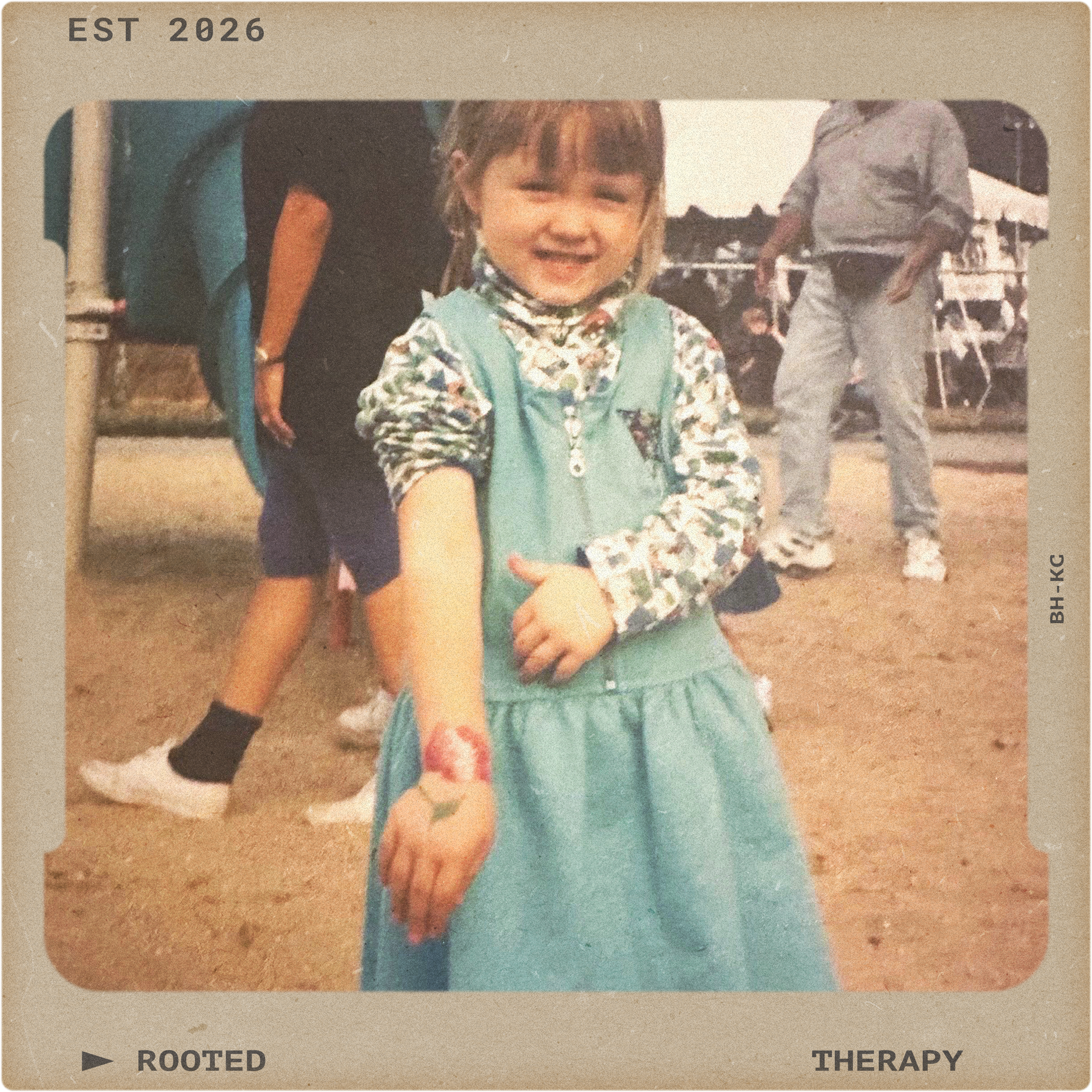 A young girl with a smile showing her arm with a fresh tattoo of a flower, standing outdoors at a themed event or fair, with other people in the background.