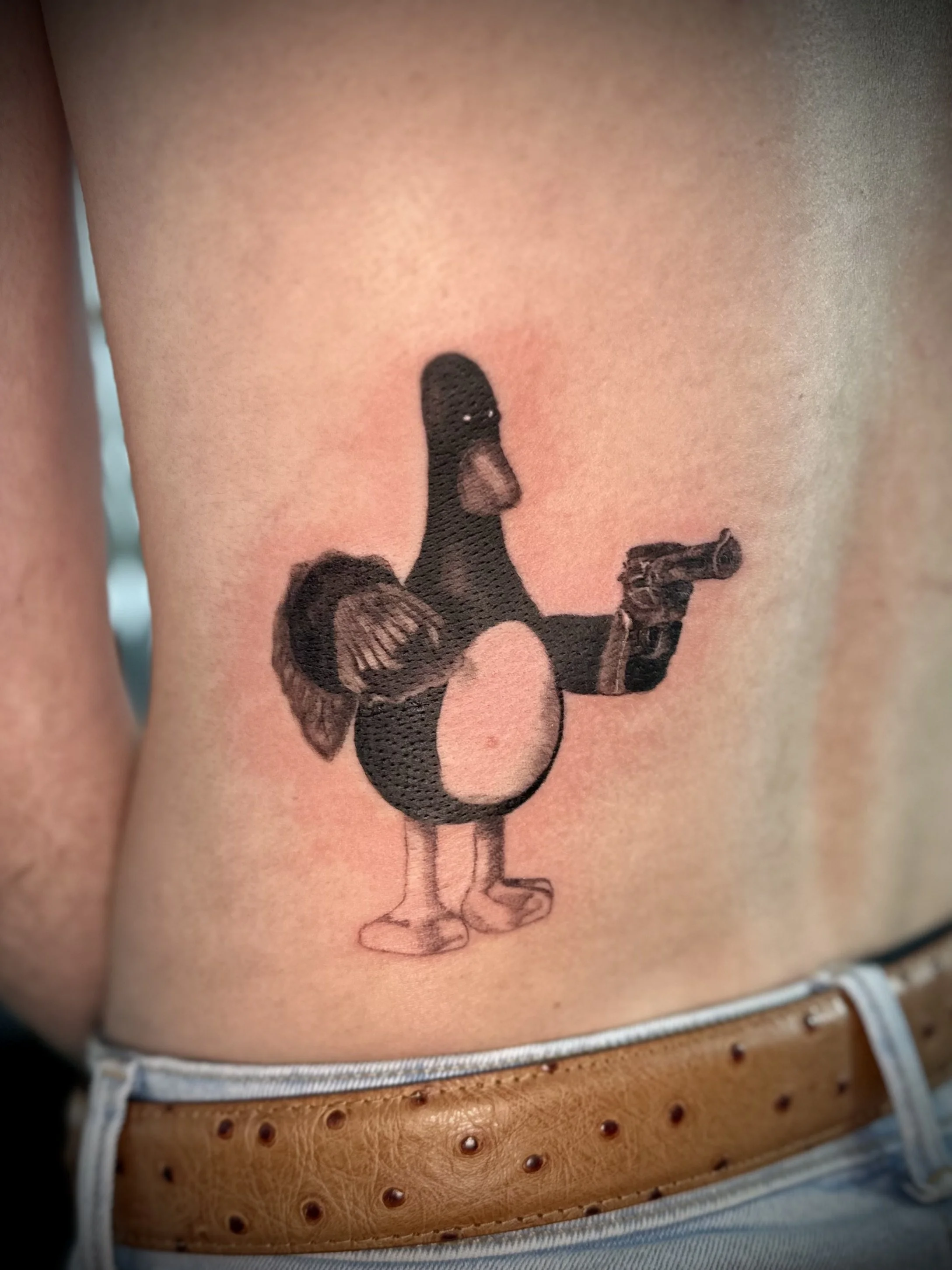 Tattoo of a bird with a humanoid body holding a gun on a person’s side.