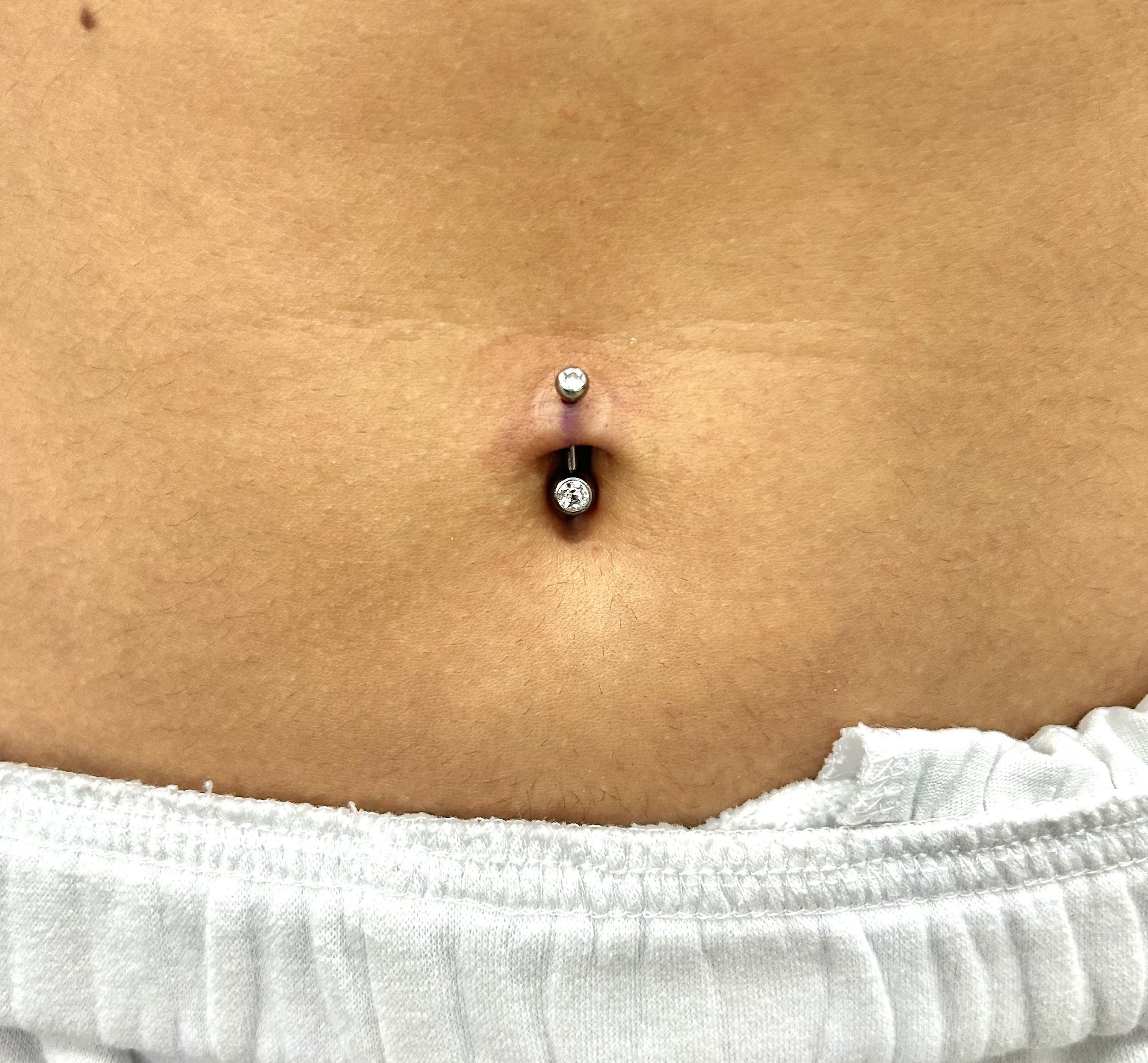 Close-up of a person's upper chest and neck with a piercing at the center of the chest, wearing white clothing.