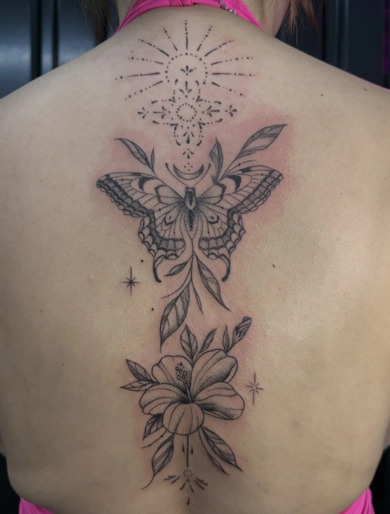 Back tattoo featuring a butterfly connected to a flower with botanical elements and decorative patterns.