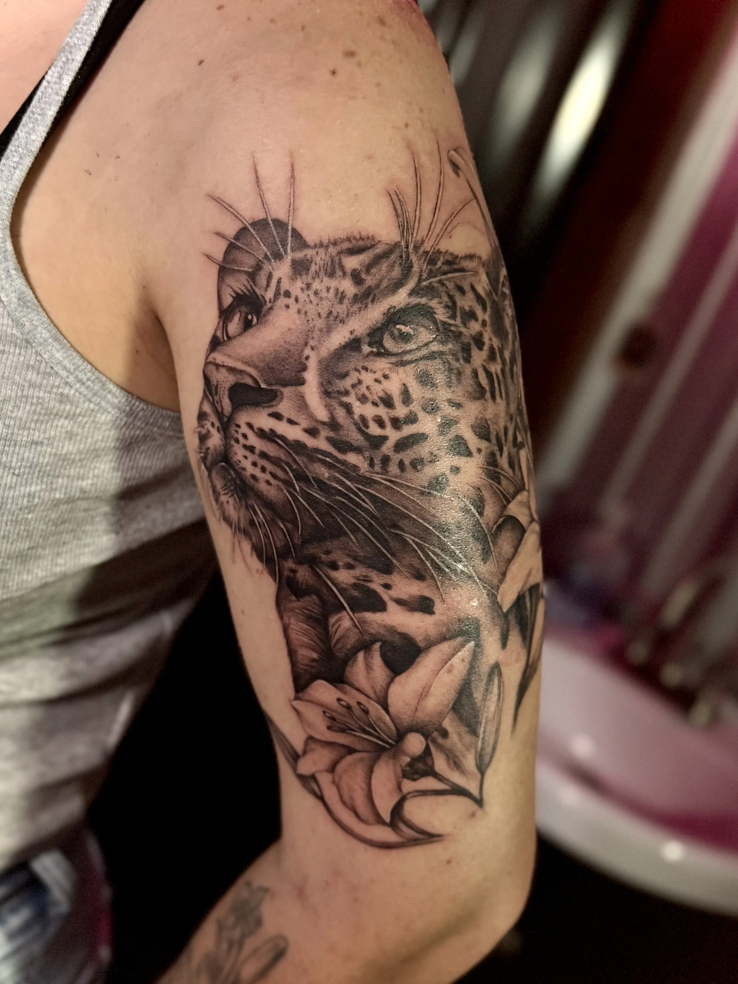 Tattoo of a leopard's face with a lily flower below on a person's upper arm.