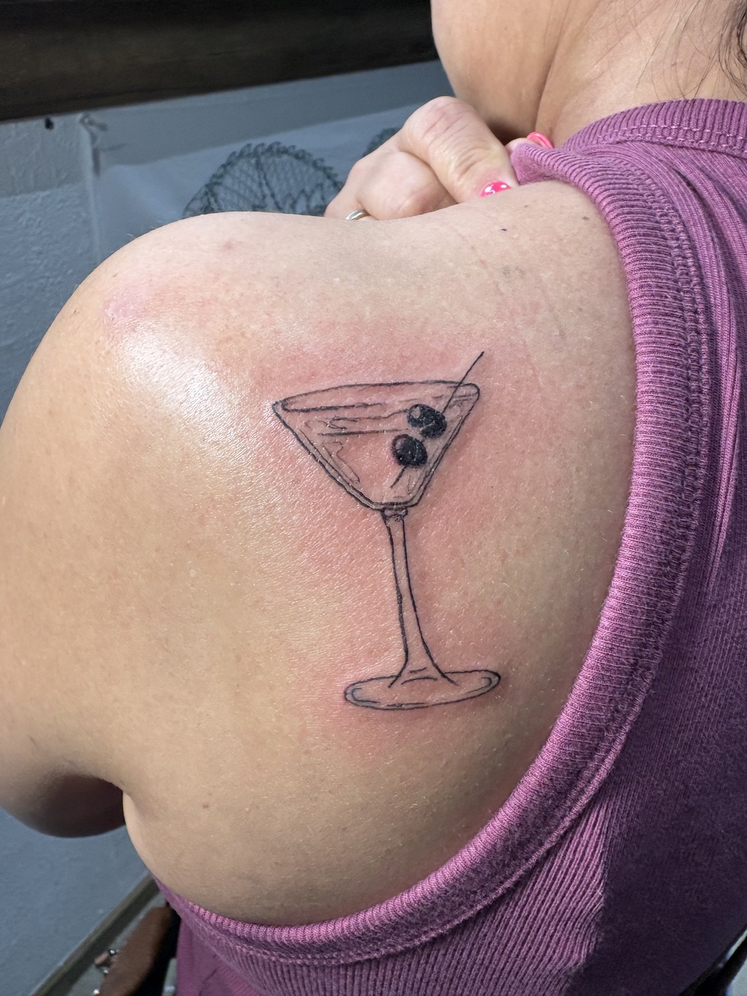 Tattoo of a martini glass with three olives on a person's upper arm.