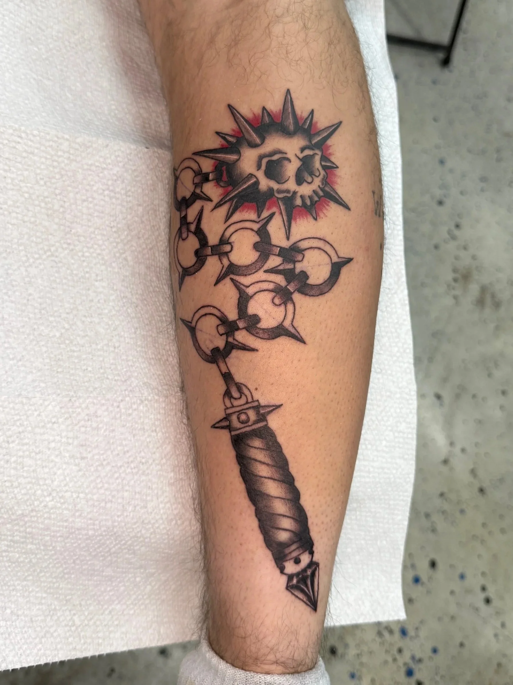 Tattoo of a spiked mace with a skull at the top, surrounded by a red background.