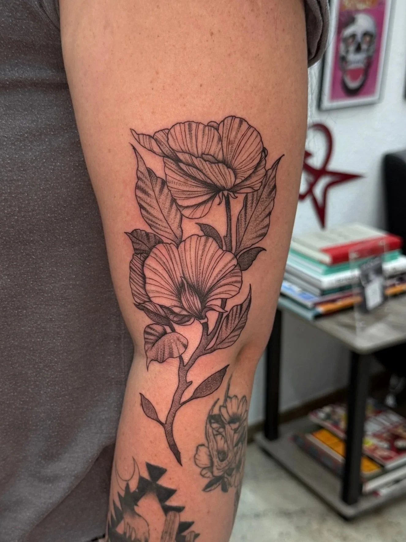 Black and gray floral tattoo of two large flowers with leaves on the arm.