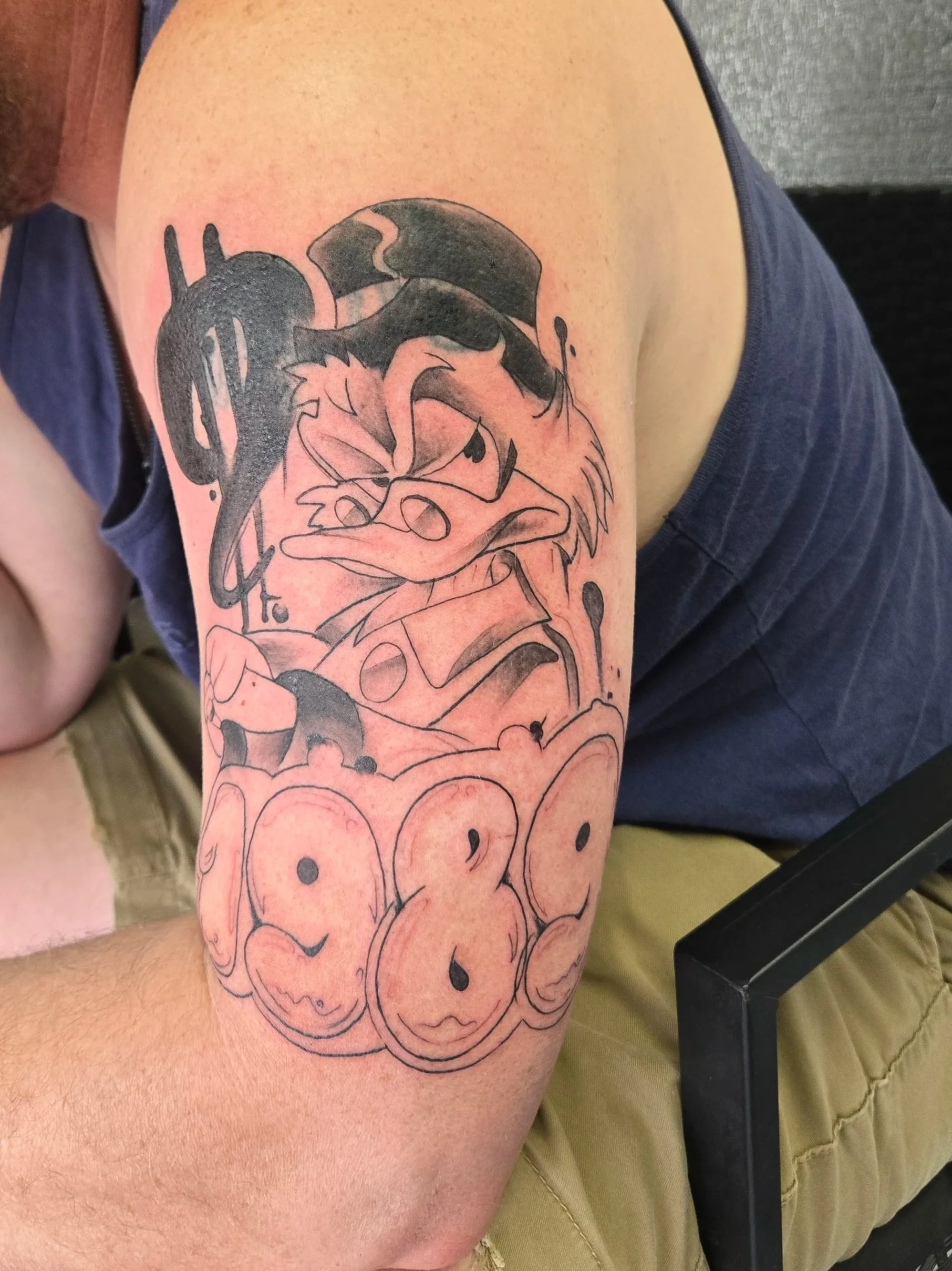 Tattoo of Scrooge McDuck wearing a hat, with the word "1989" in bubble letters below.