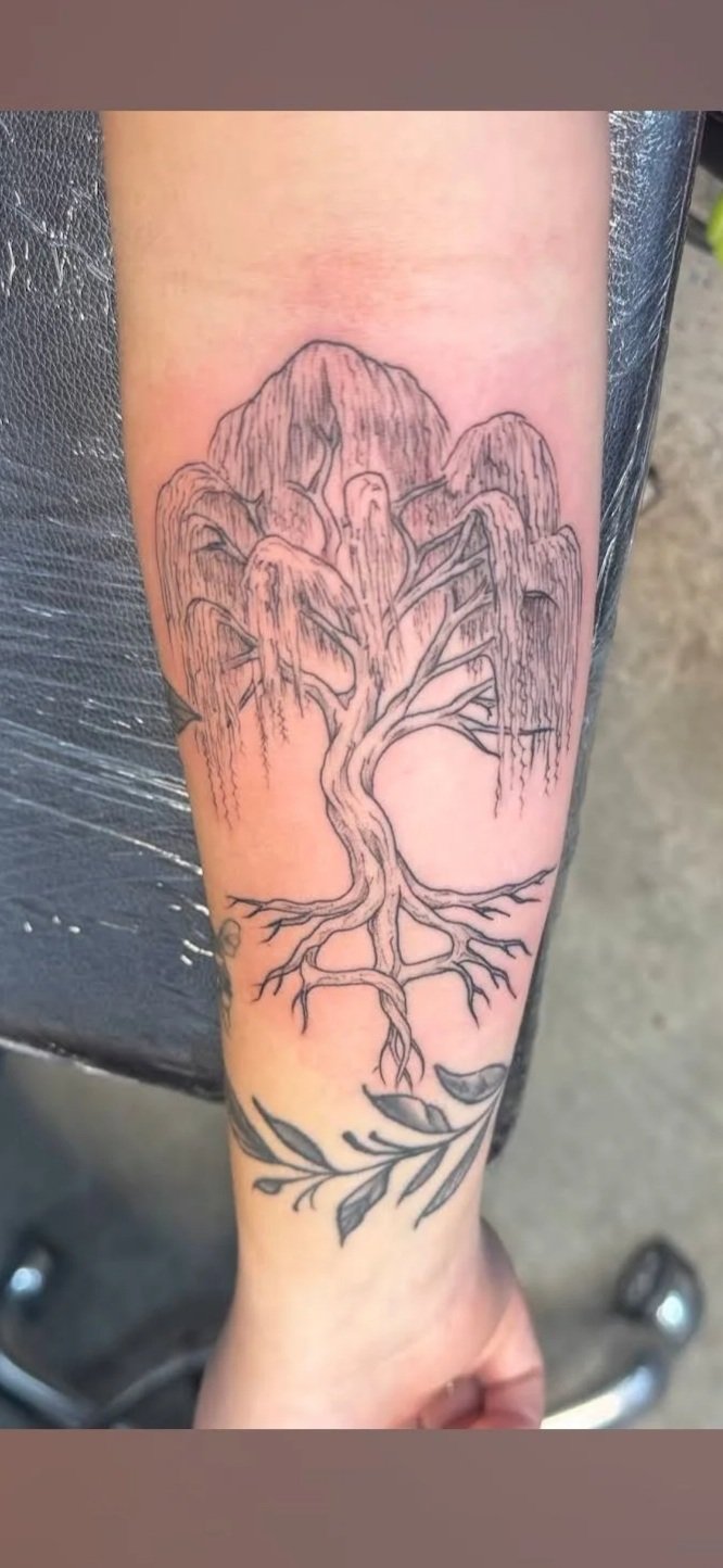 Line art tattoo of a tree with roots, branches, and leaves on a person's forearm.